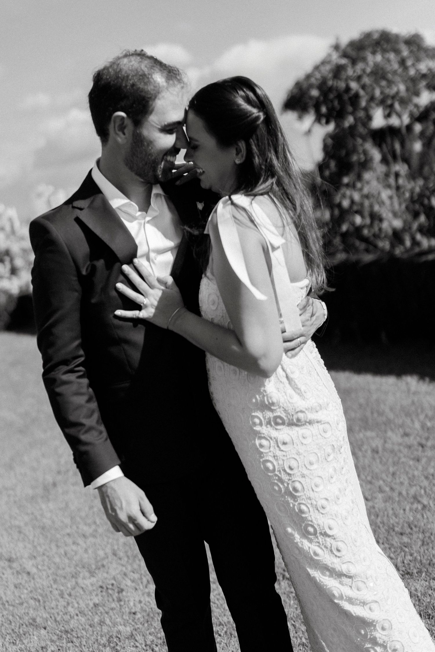 Black and white photo of a bride and groom sharing an intimate moment outdoors, with the bride in a lace gown.