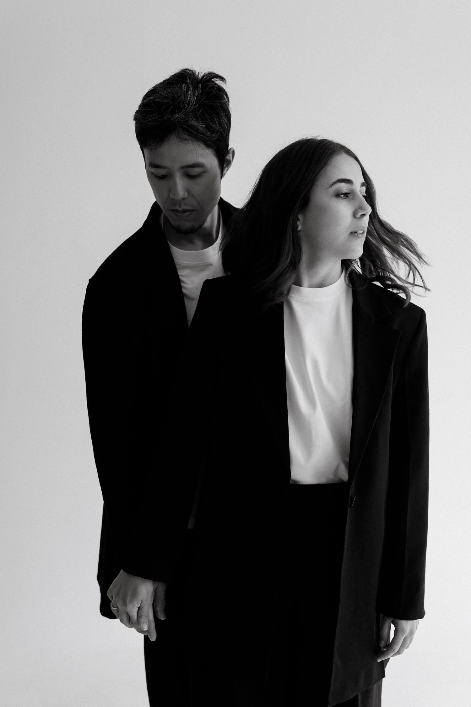 Black and white portrait of a man and woman in black blazers posing together against a light background.