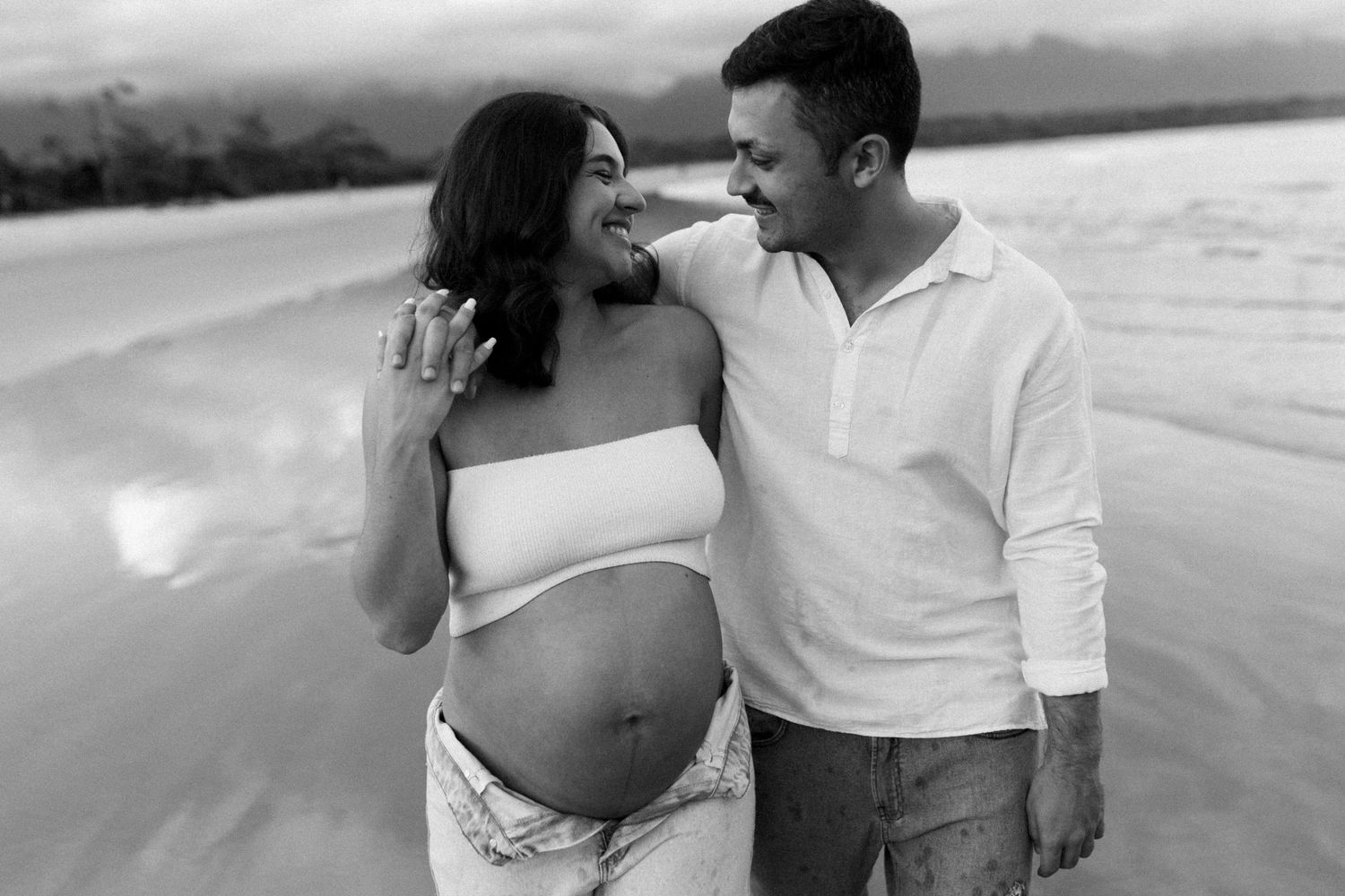 Romantic black and white beach photos of couple embracing on sandy shore.