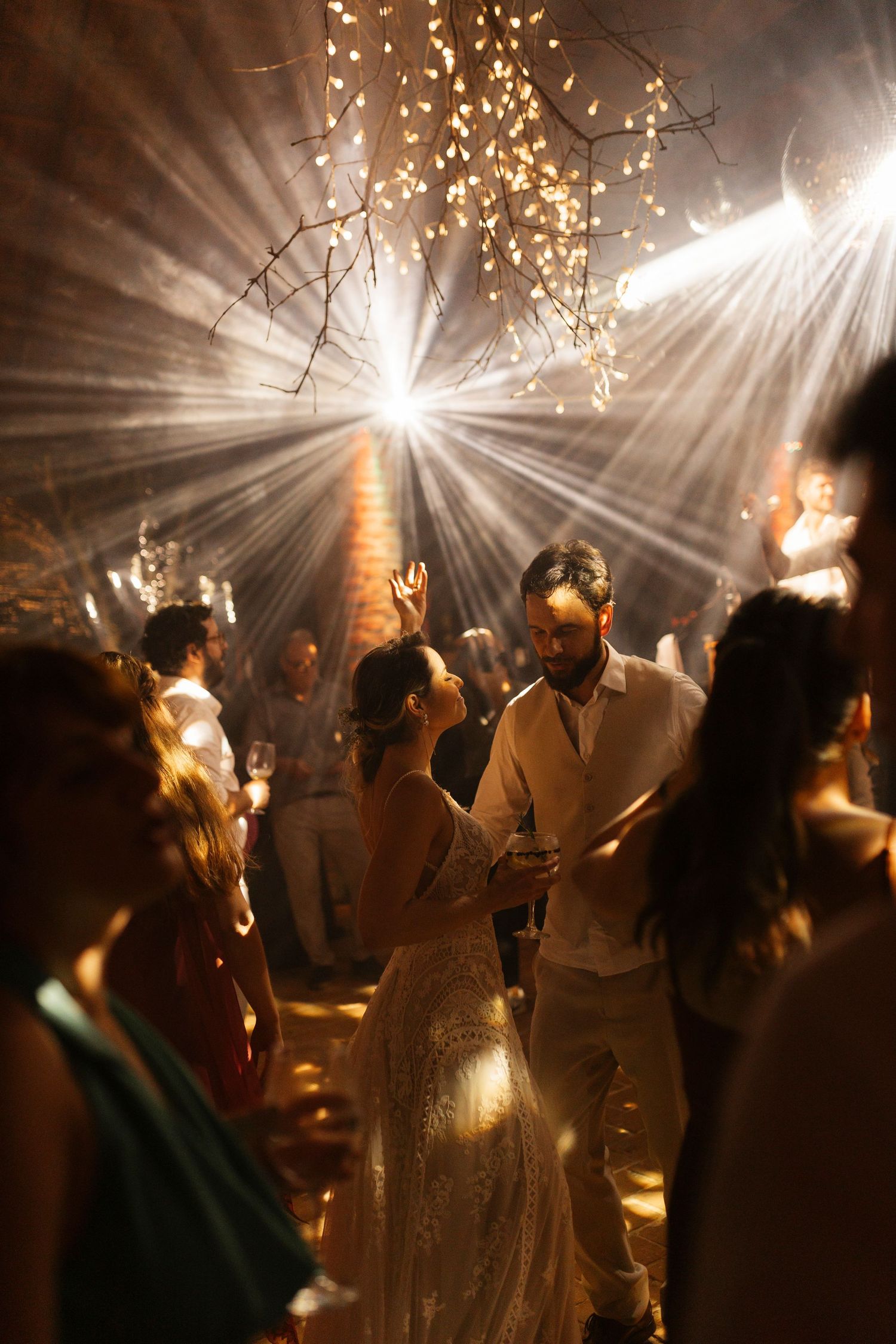 Wedding reception dance floor with string lights creating magical atmosphere and silhouettes of dancing guests.