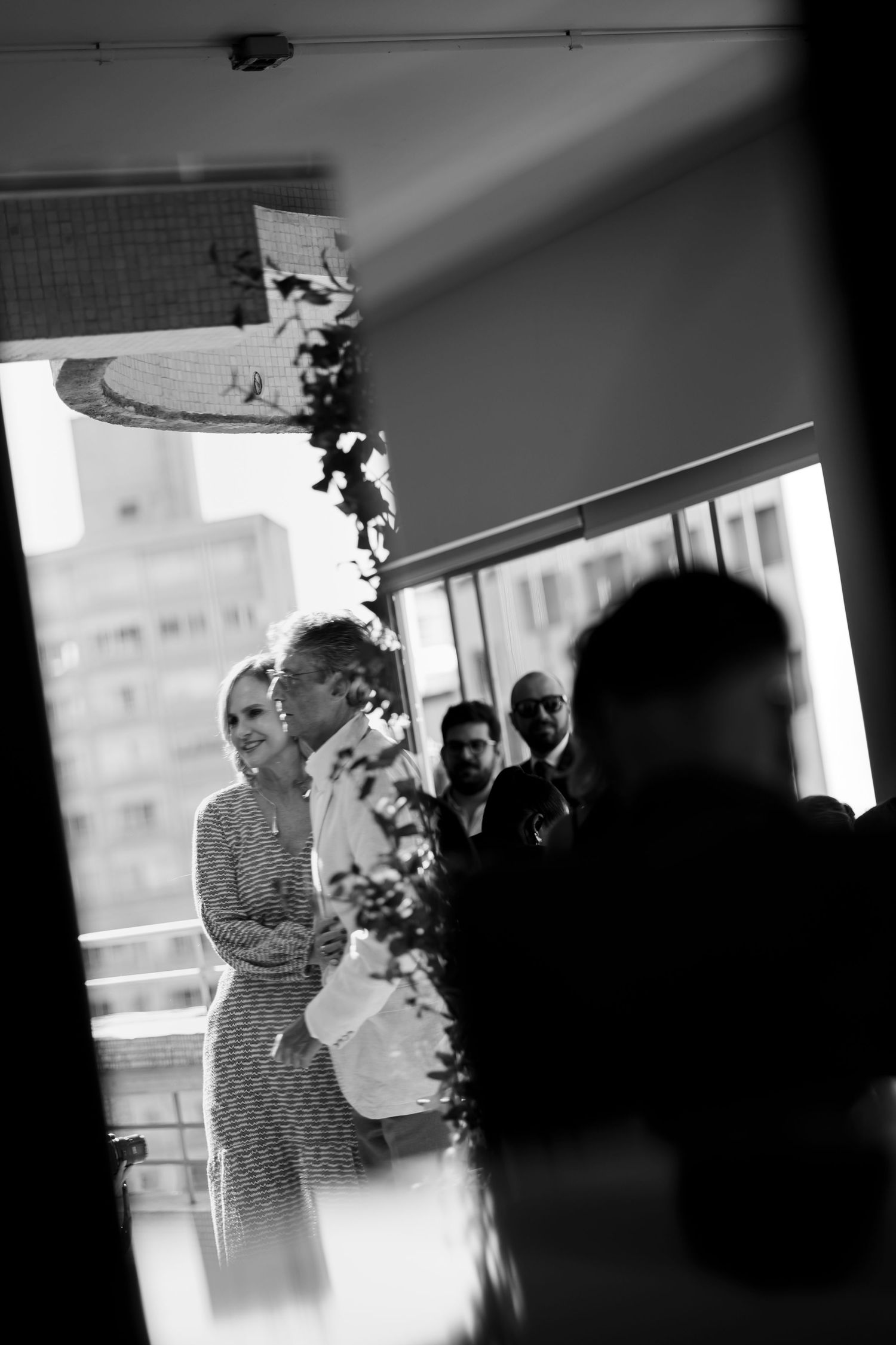 Black and white silhouettes of people gathering near a window in an interior space.