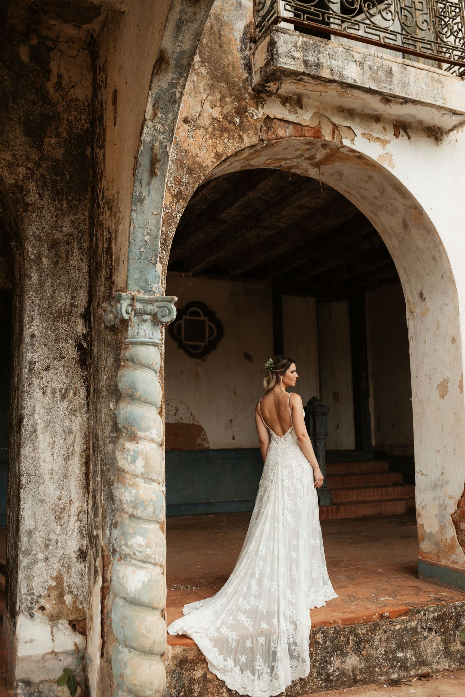 Bride in lace wedding gown poses elegantly through series of rustic archways.