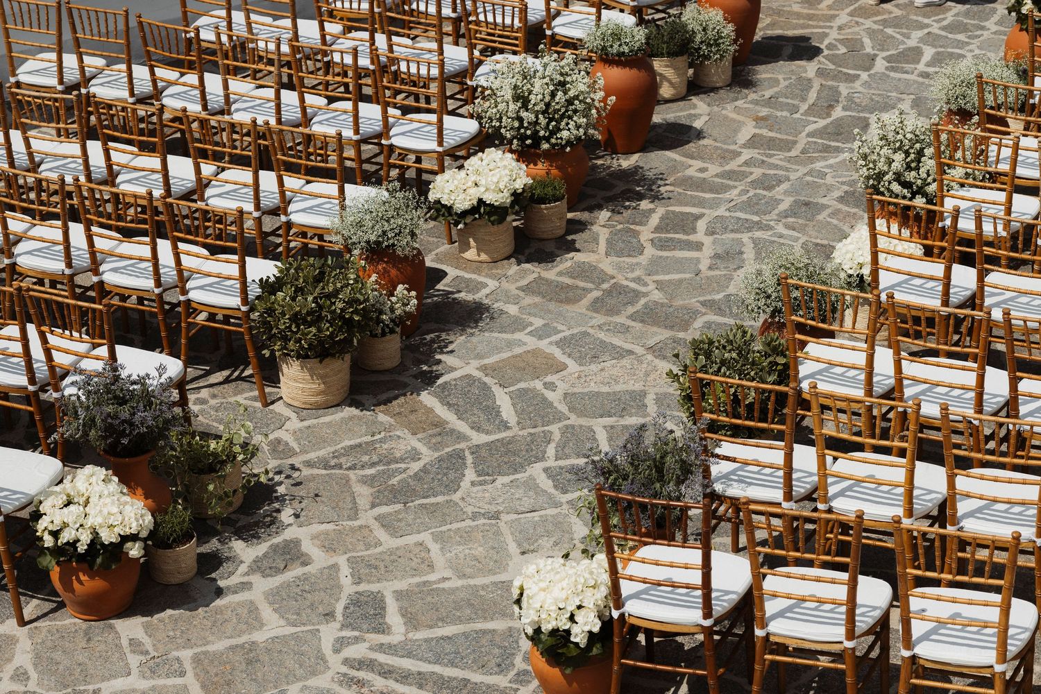 Wooden chairs arranged in rows on a stone patio for an outdoor ceremony.