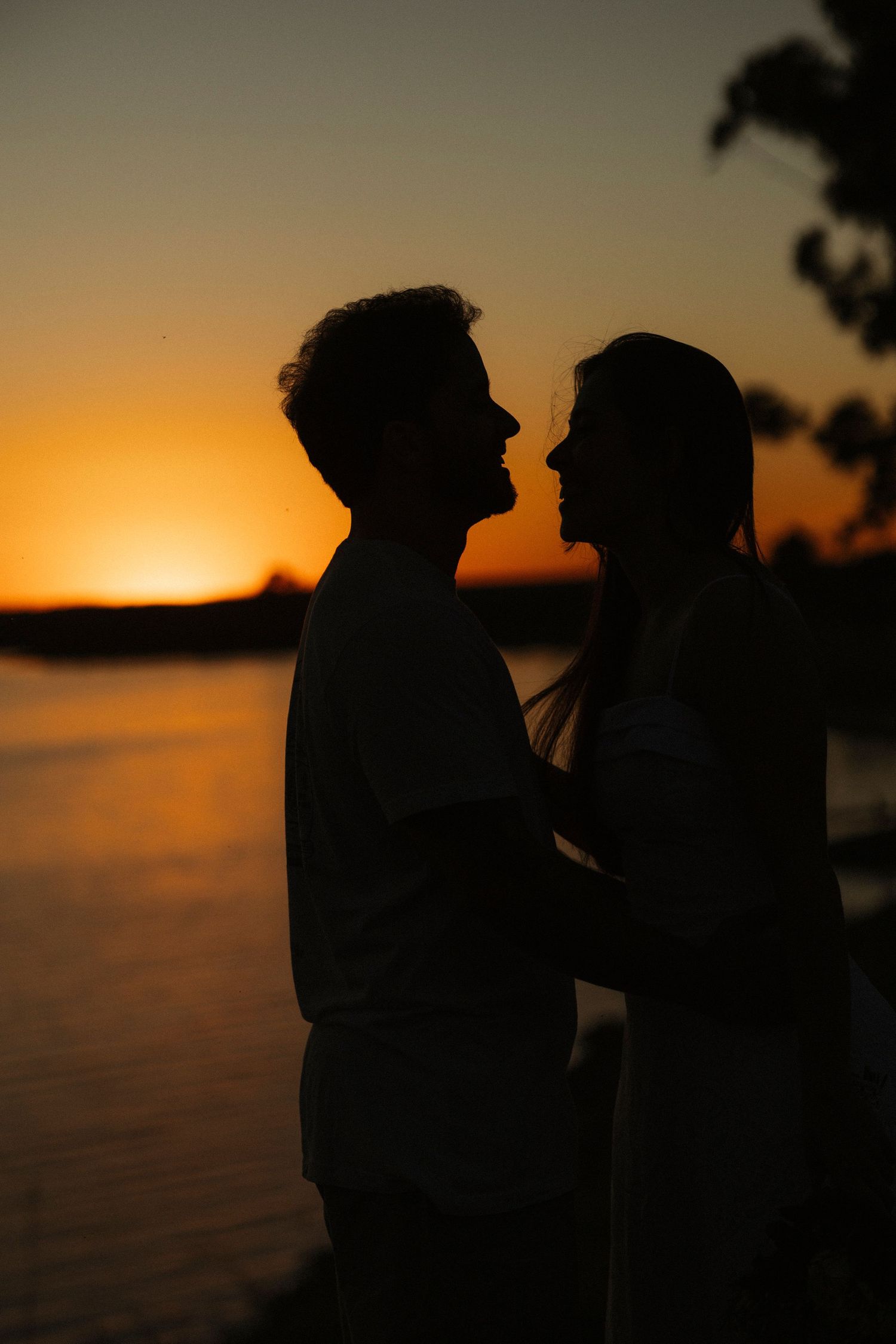 Silhouettes of couple against dramatic orange sunset over water.