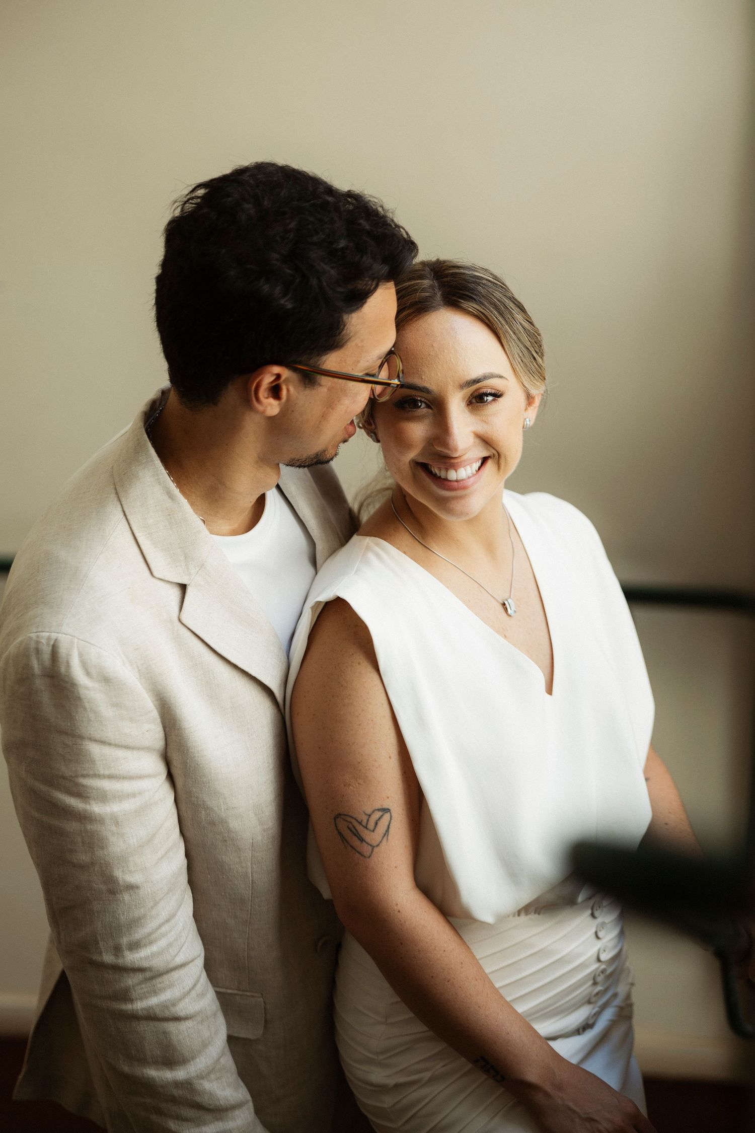 Intimate couple in white attire sharing tender moments against neutral background.