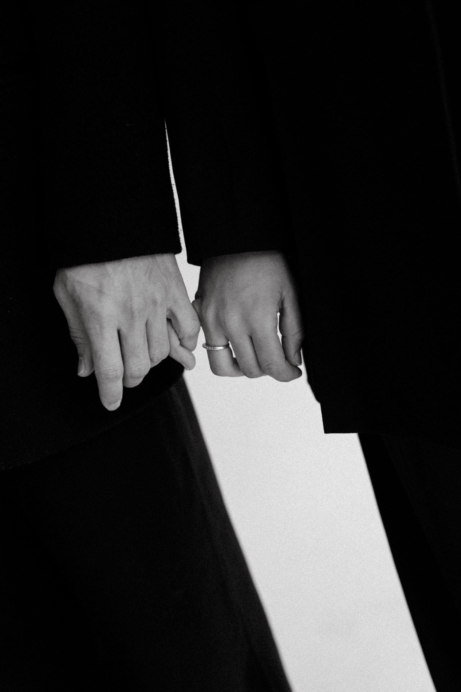 Black and white photo of hands holding white papers, one hand wearing a ring, dressed in dark formal attire.