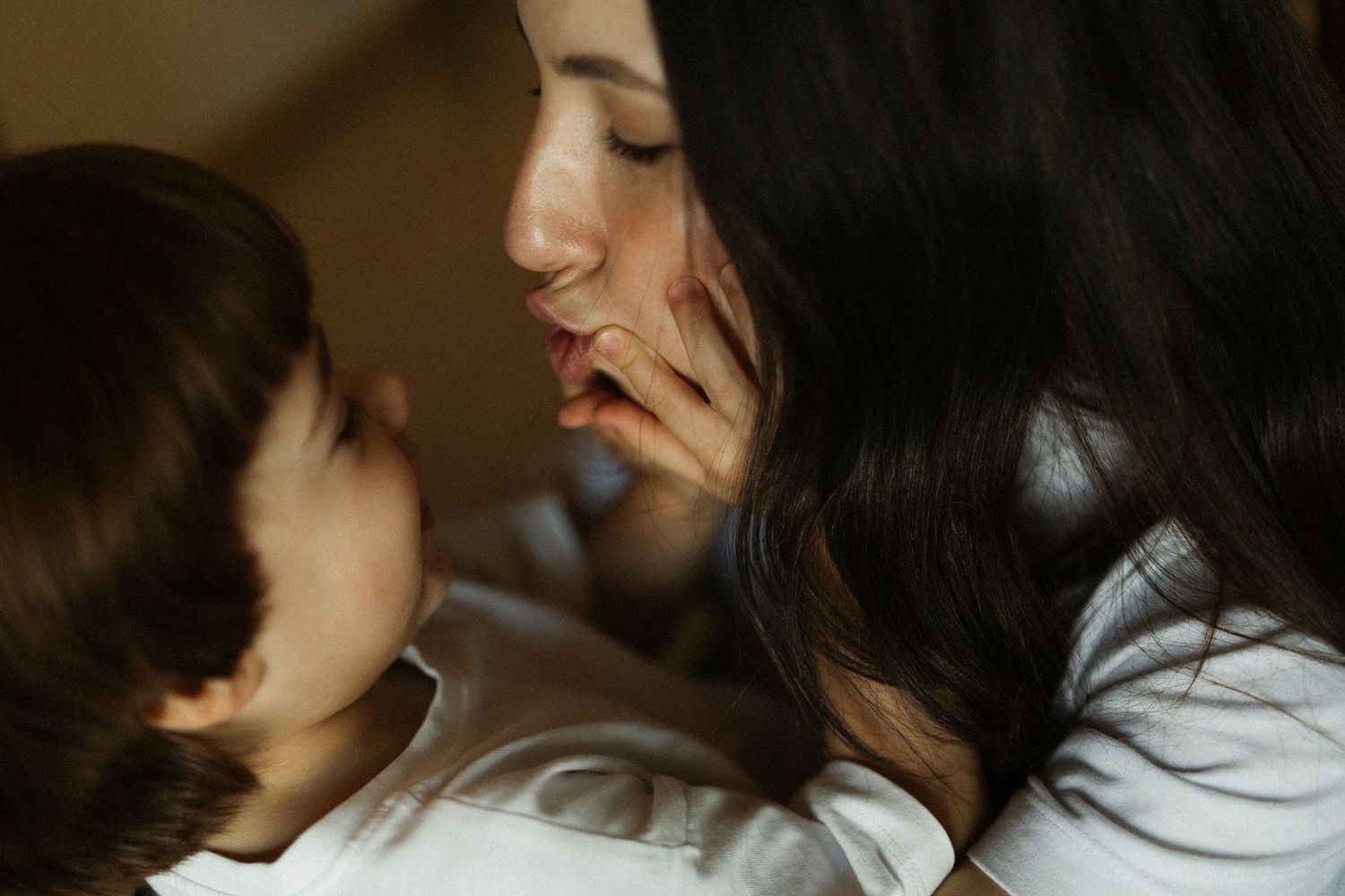 A tender moment between a mother and young child, their faces close together in warm, soft lighting.