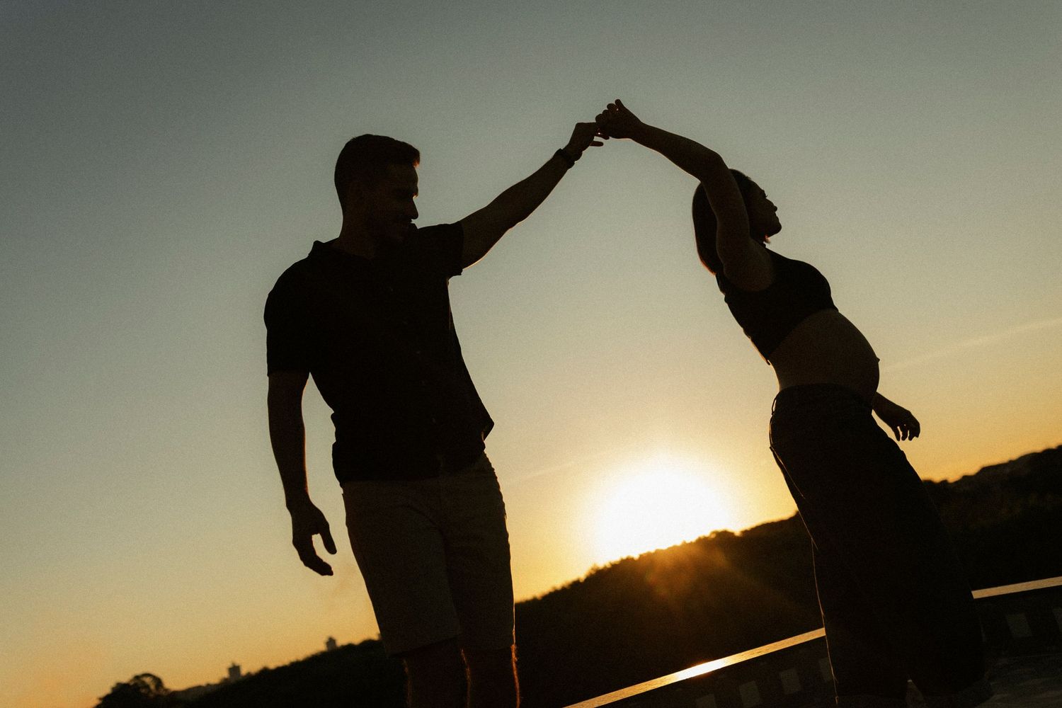 Silhouette of a couple dancing and holding hands against a vibrant golden sunset sky.