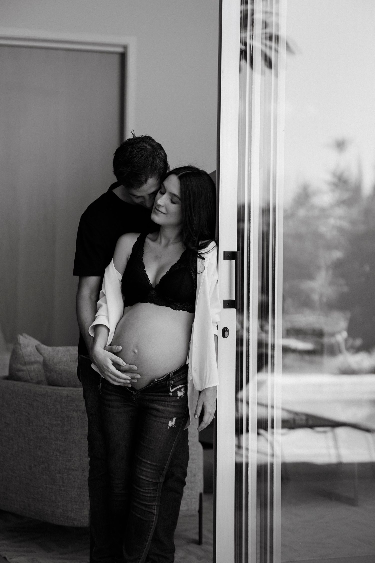 Intimate black and white maternity photo by glass doors.