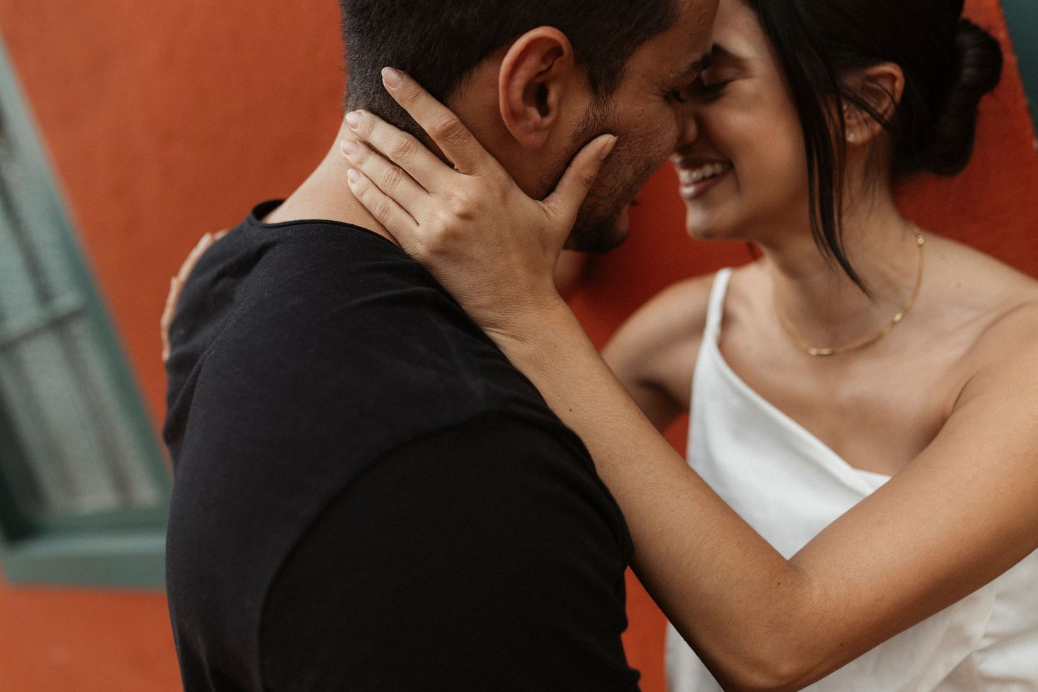 A romantic couple in formal attire share an intimate embrace against a warm-toned background.