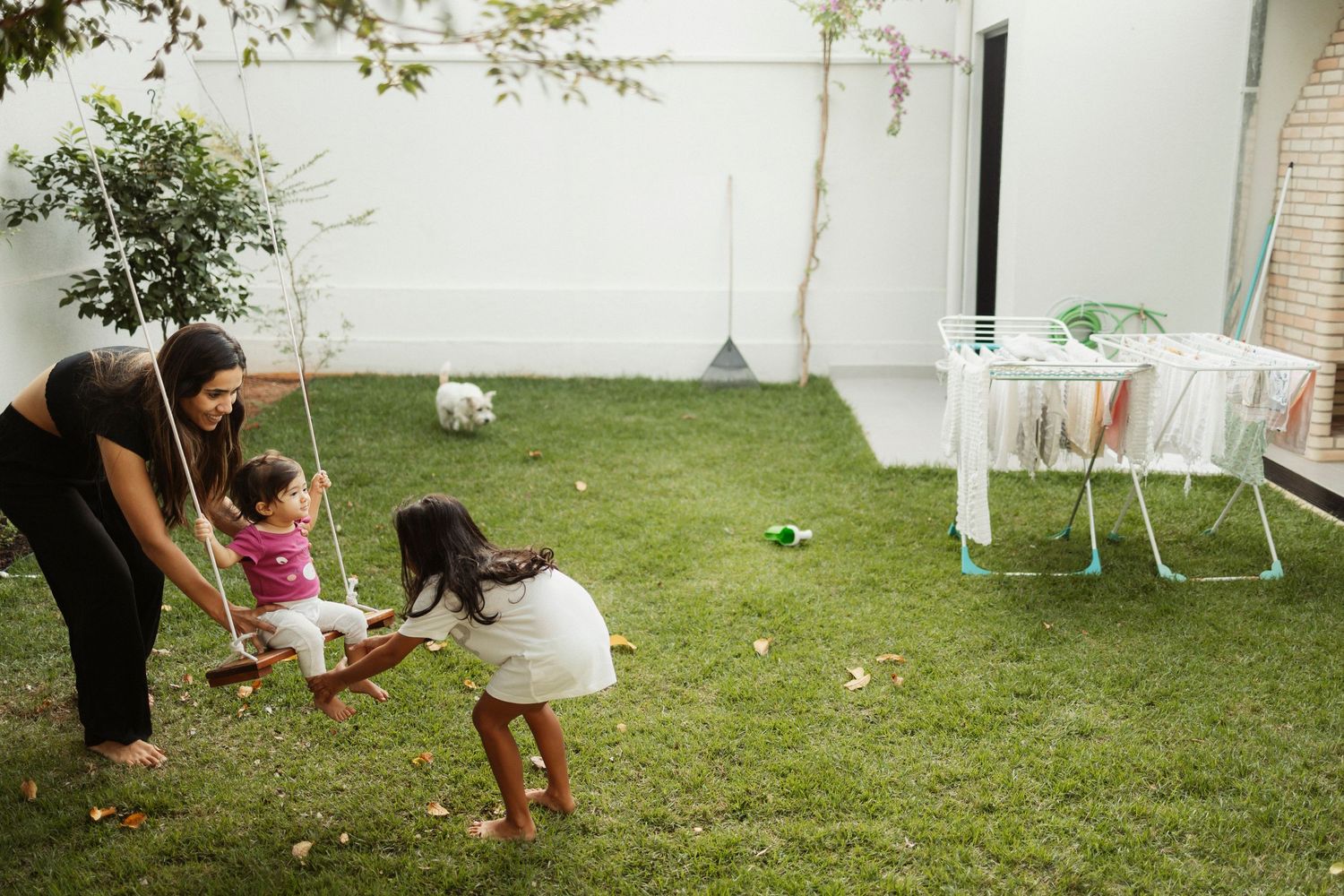 People playing and relaxing in a backyard with white walls and green grass.