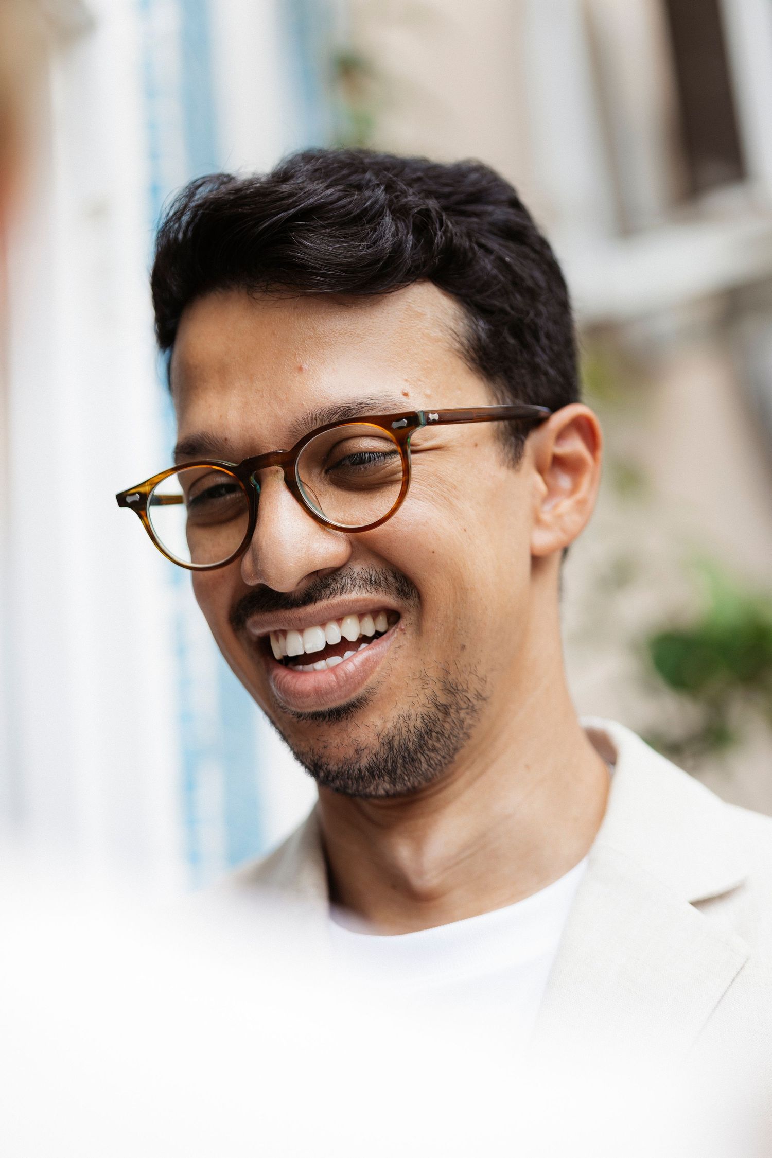 Joyful person in glasses and white shirt smiling warmly at the camera in a series of candid portraits.