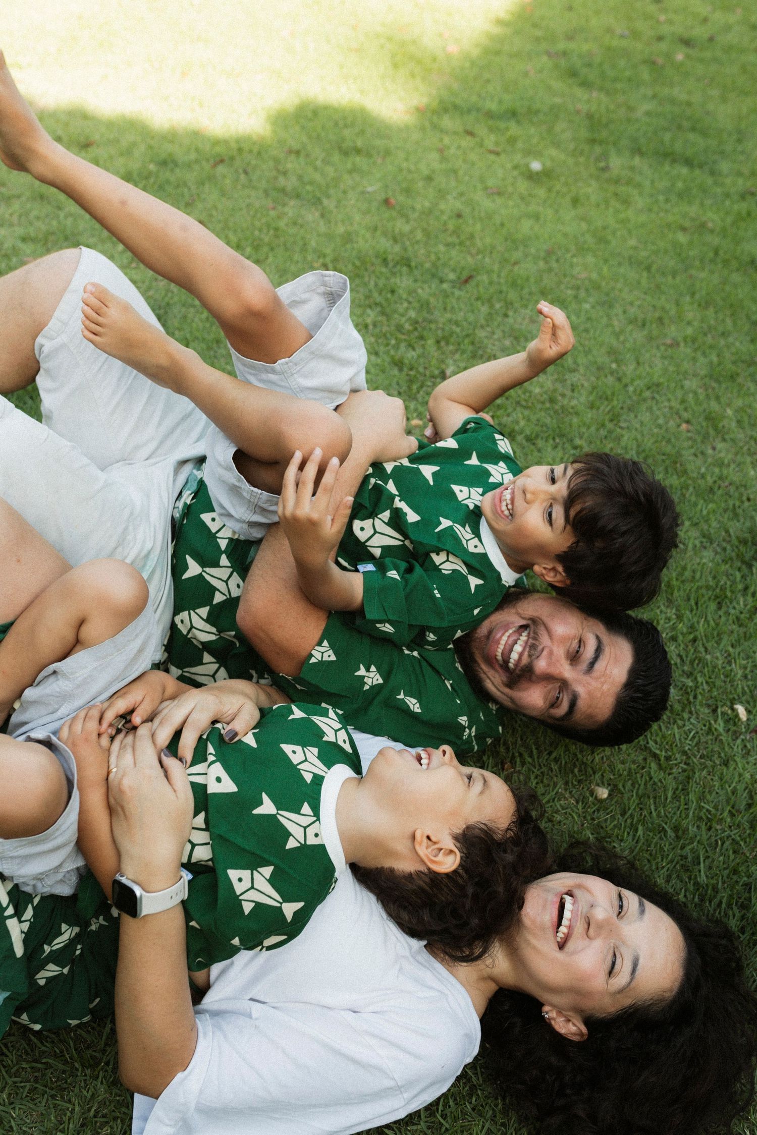 Two people lying on green grass laughing and playing together in casual summer outfits.