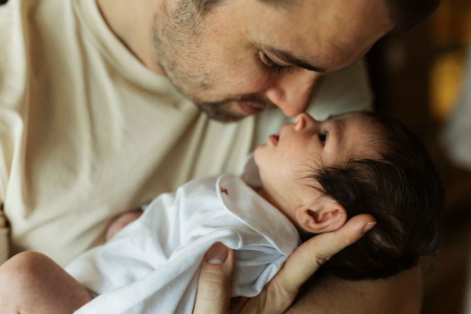 A tender moment as a father gently nuzzles his newborn baby wrapped in a white blanket.