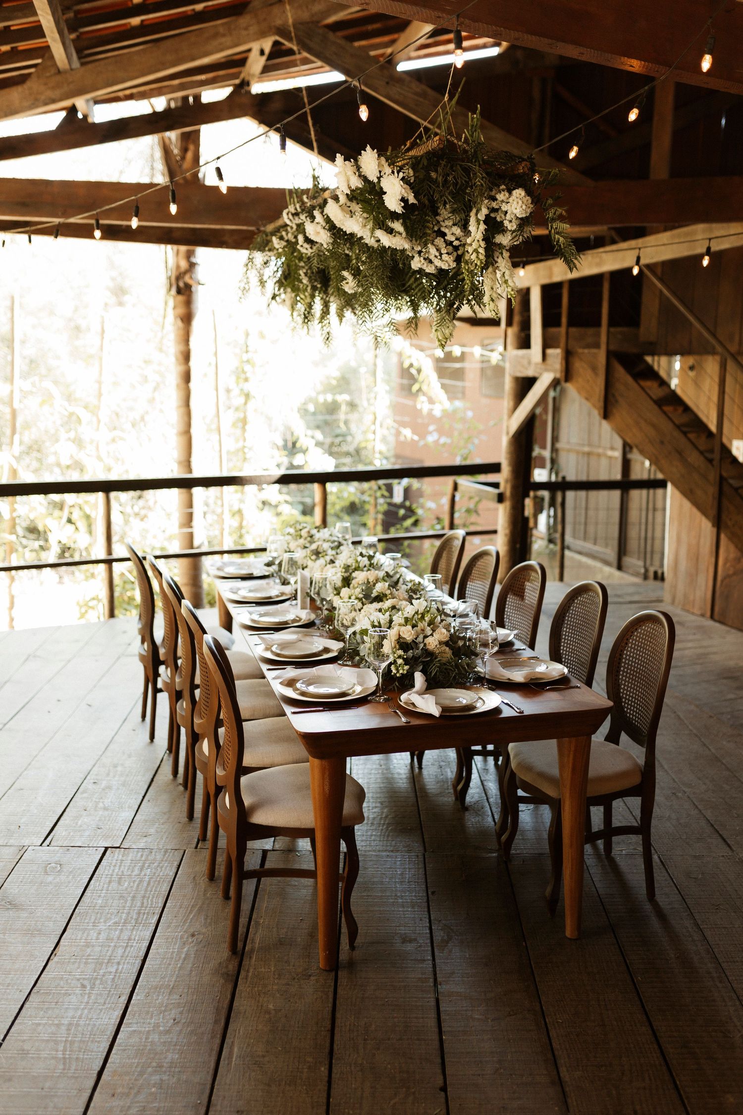 Rustic barn reception venue with elegant table settings and hanging greenery decorations.