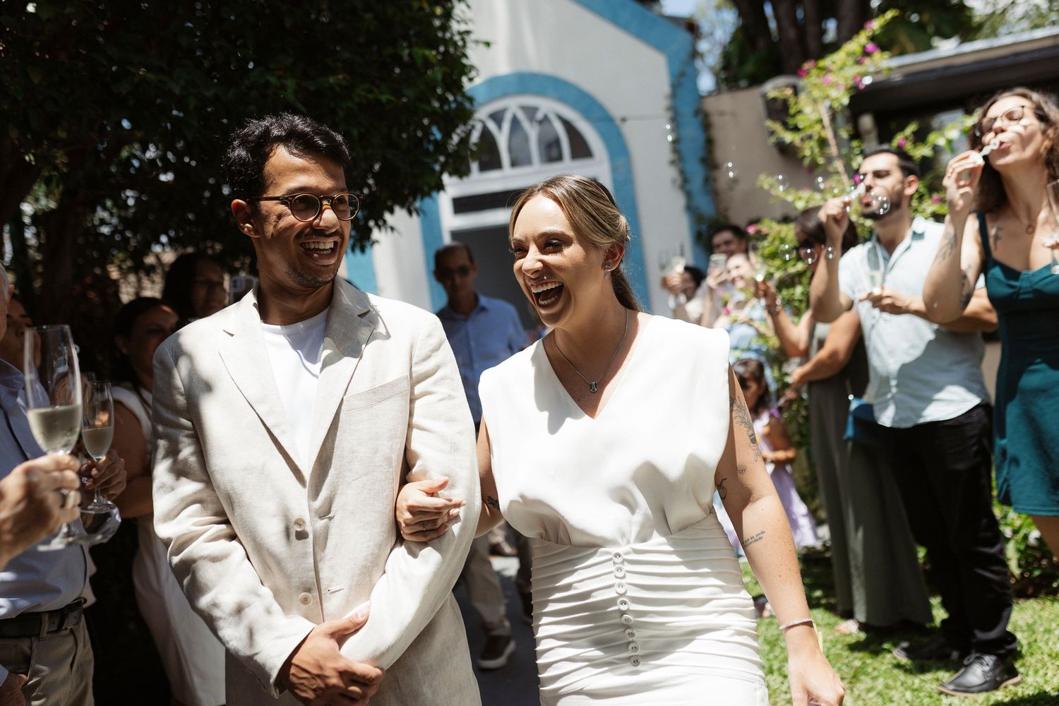 Newlyweds celebrate with guests in sunny outdoor garden setting.