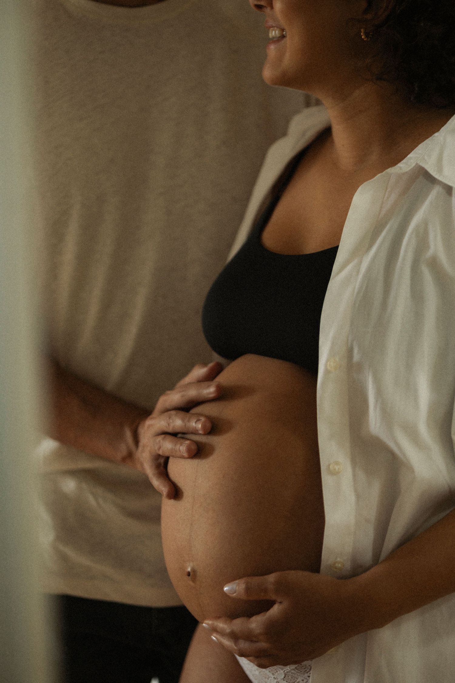 Maternity portrait showing pregnant belly with woman wearing white button-down shirt.