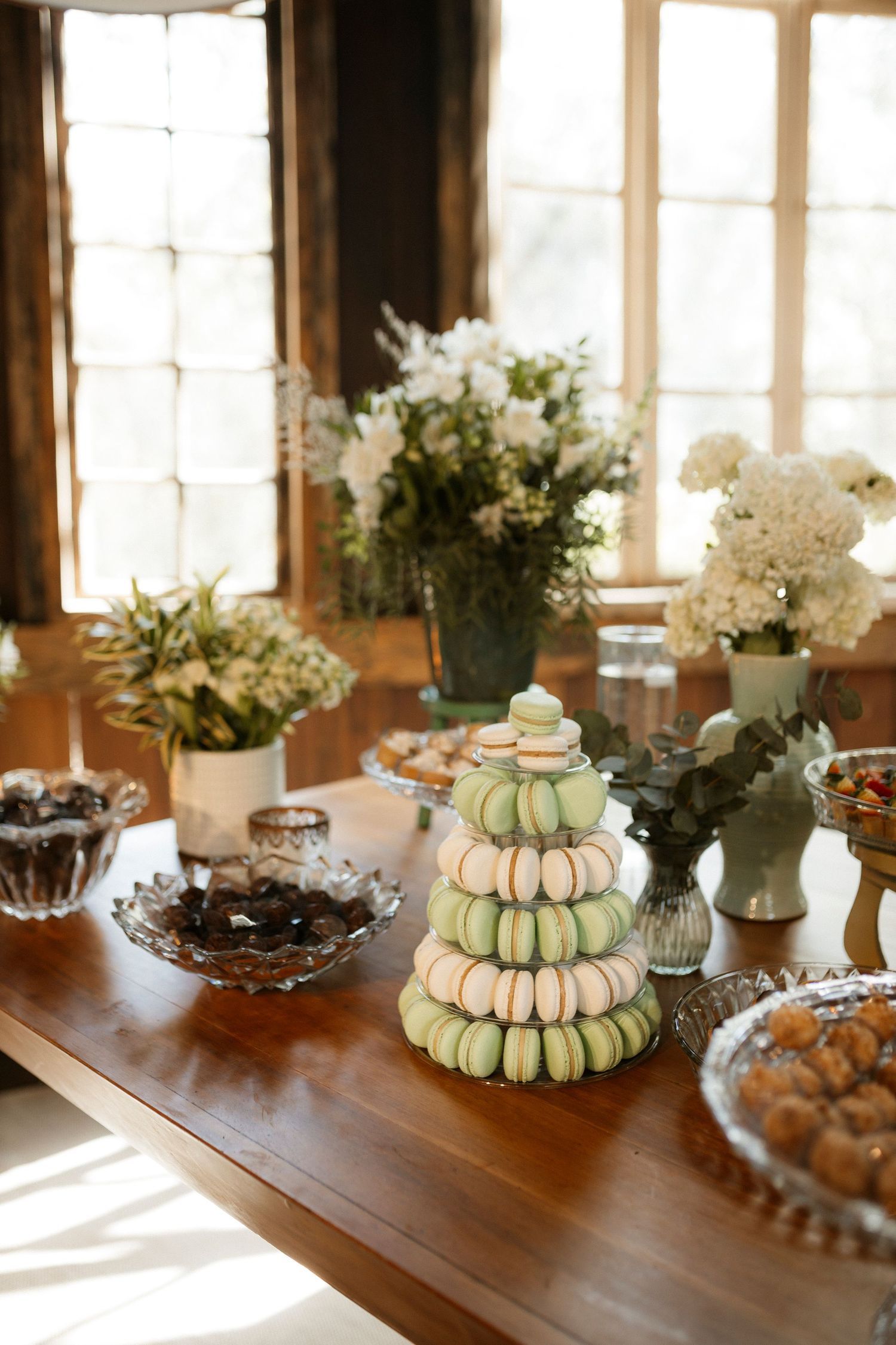 Elegant table setting with white floral arrangements and stacked macarons in sunlit room.