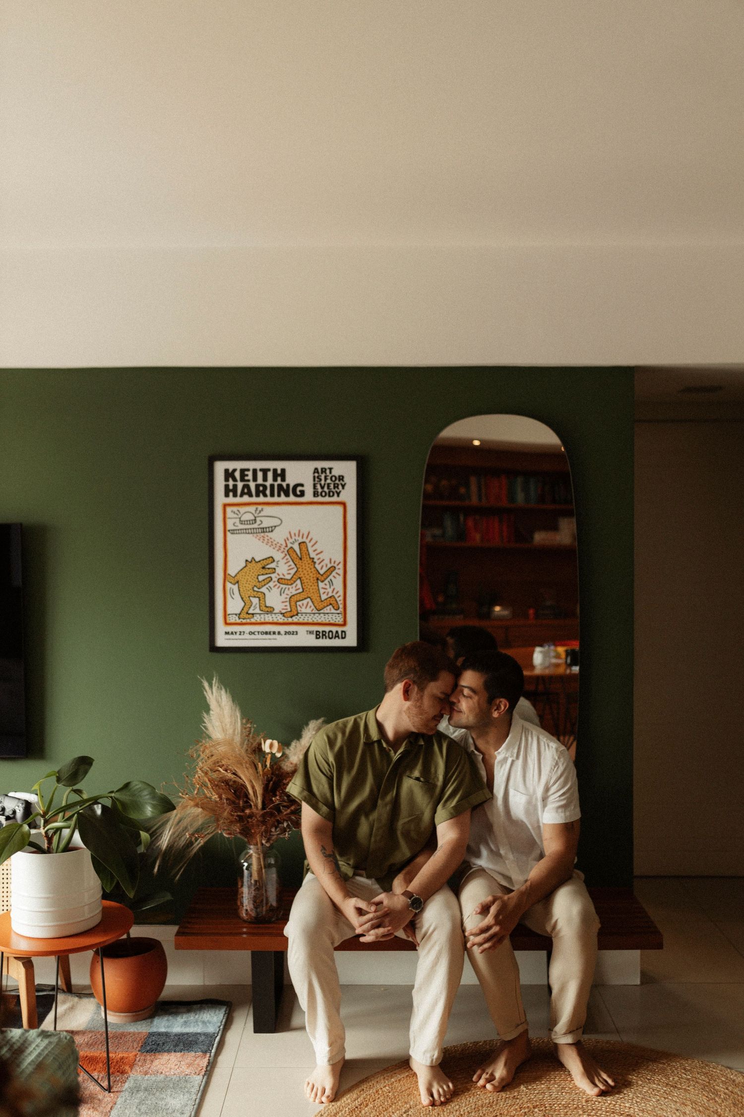 Two people sitting on couch in room with green walls and vintage posters.