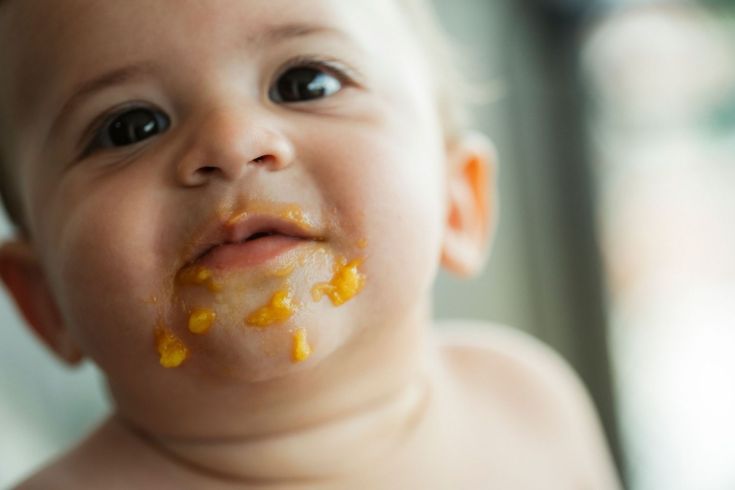 A baby with messy food around their mouth smiles in a series of close-up photos.