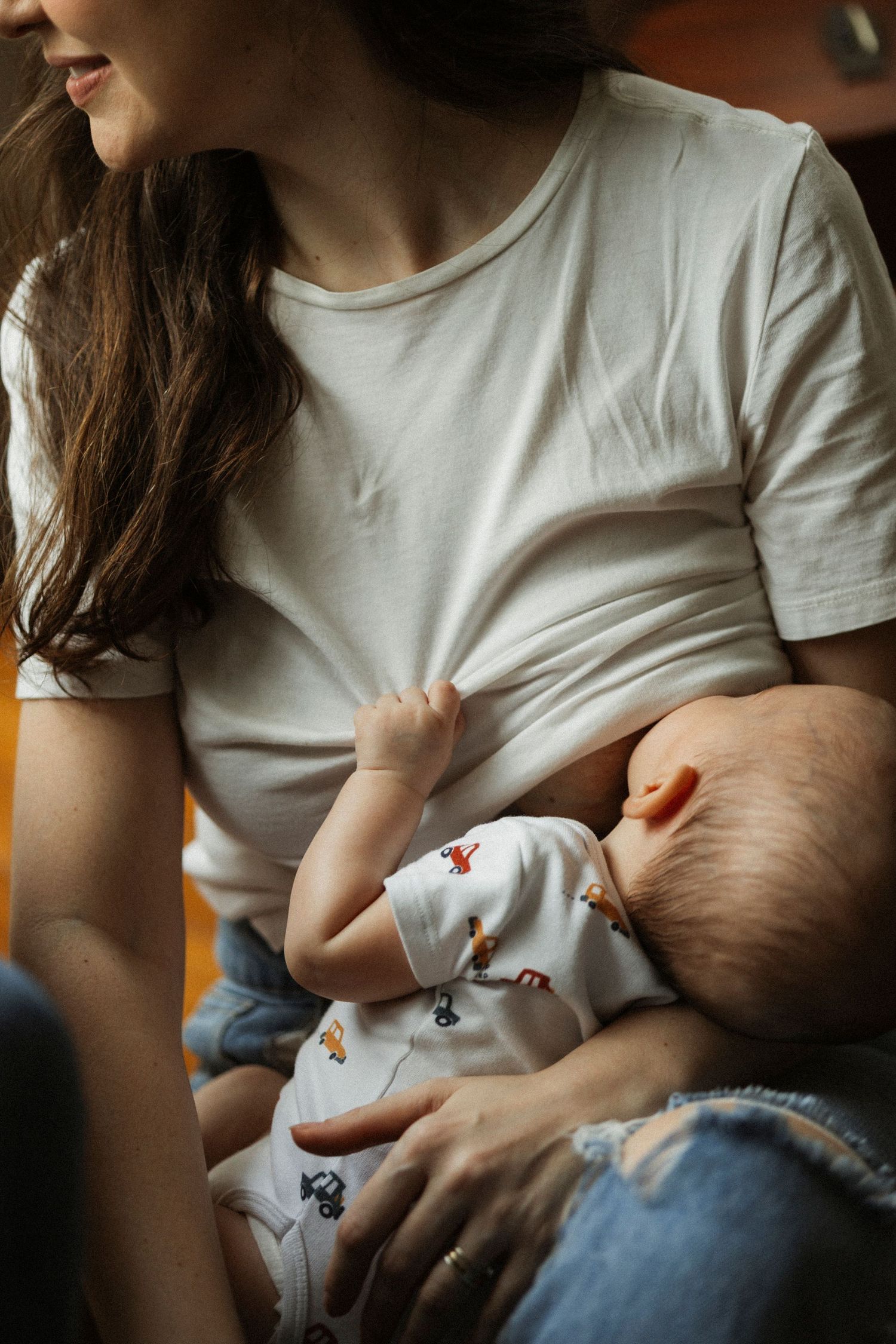 A mother in a white t-shirt and jeans breastfeeding her newborn baby dressed in a patterned onesie.
