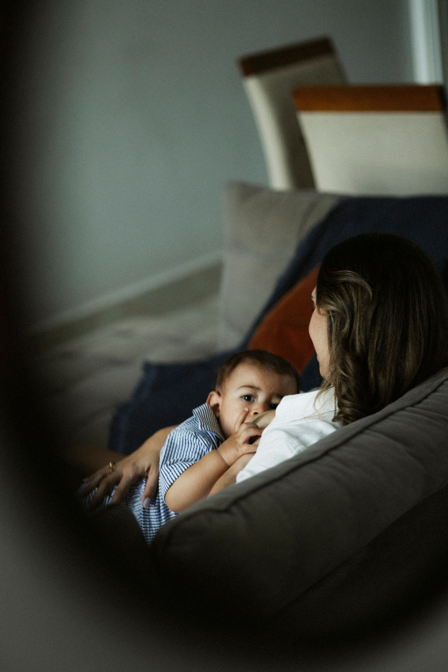 Mother breastfeeding her baby boy on a couch, captured through a mirror reflection in a cozy home setting.