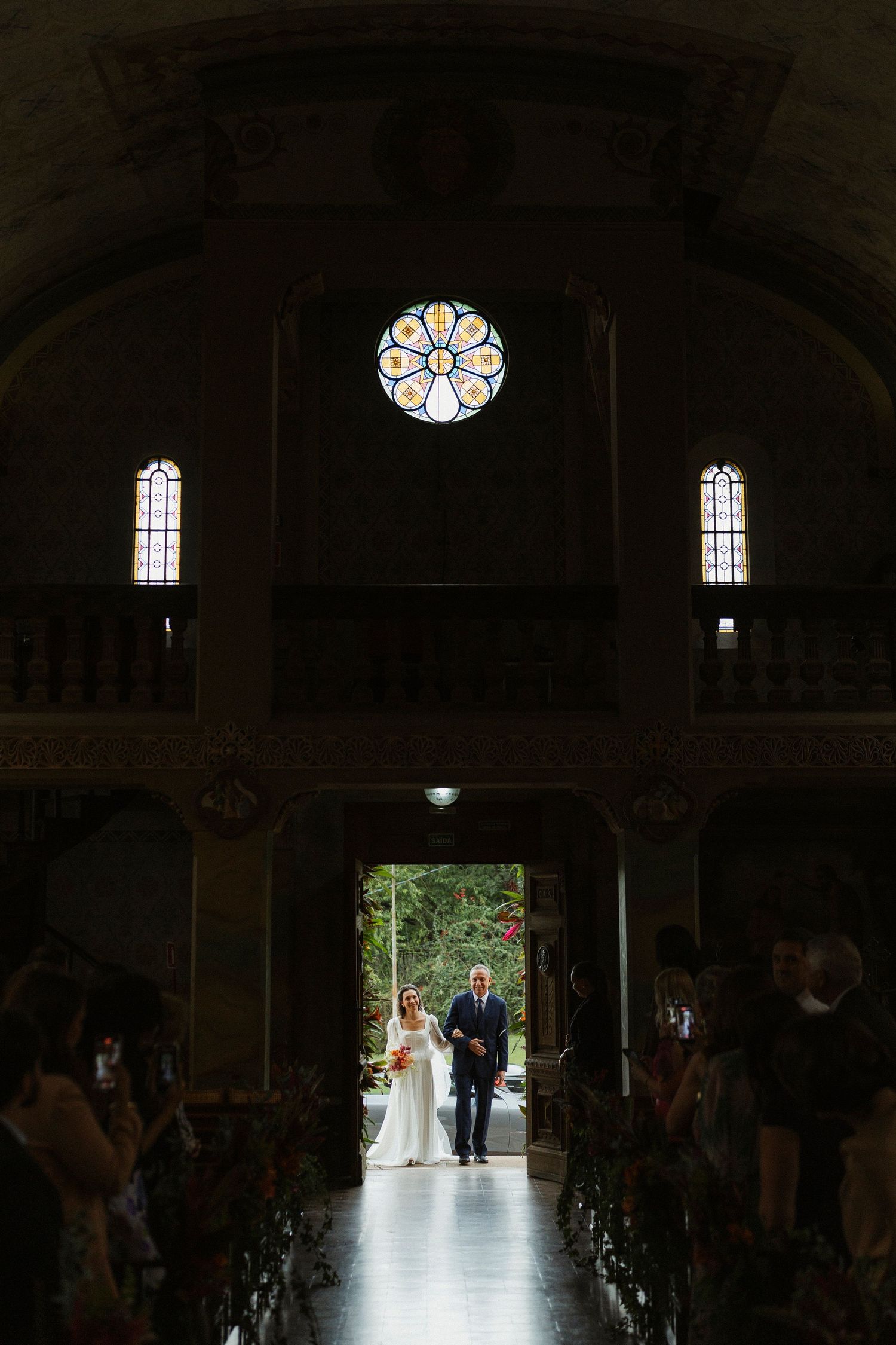 Bride walks down the aisle with her father in a stunning church wedding ceremony with rose window.