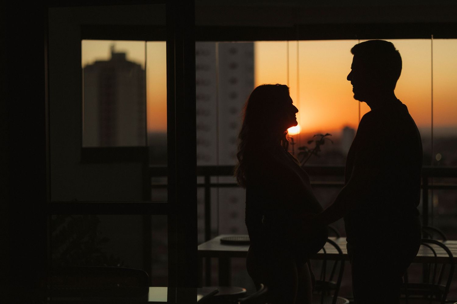 Silhouettes against sunset sky through window creating dramatic urban scene.