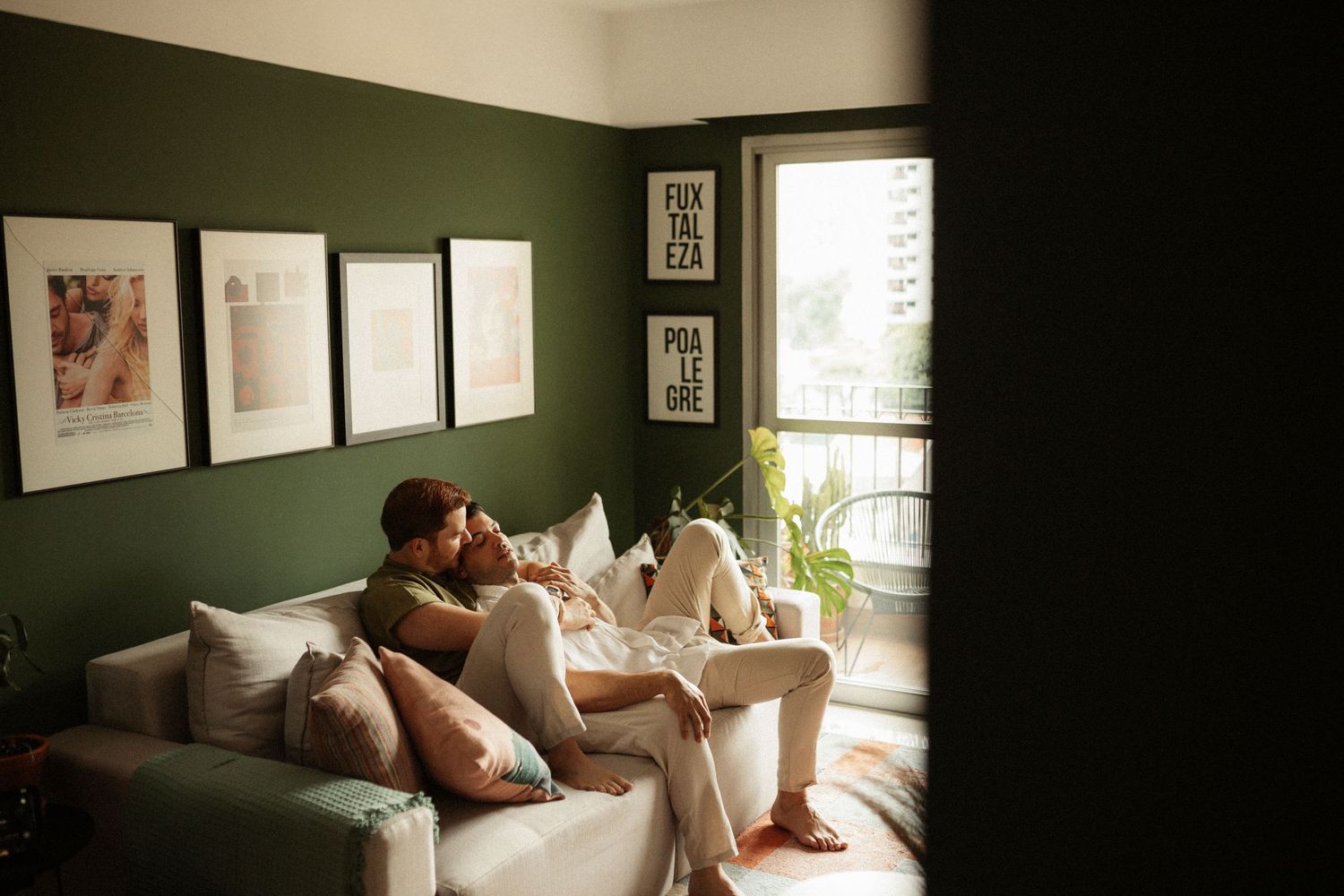 Couple resting together on a couch in a dimly lit room with natural light.