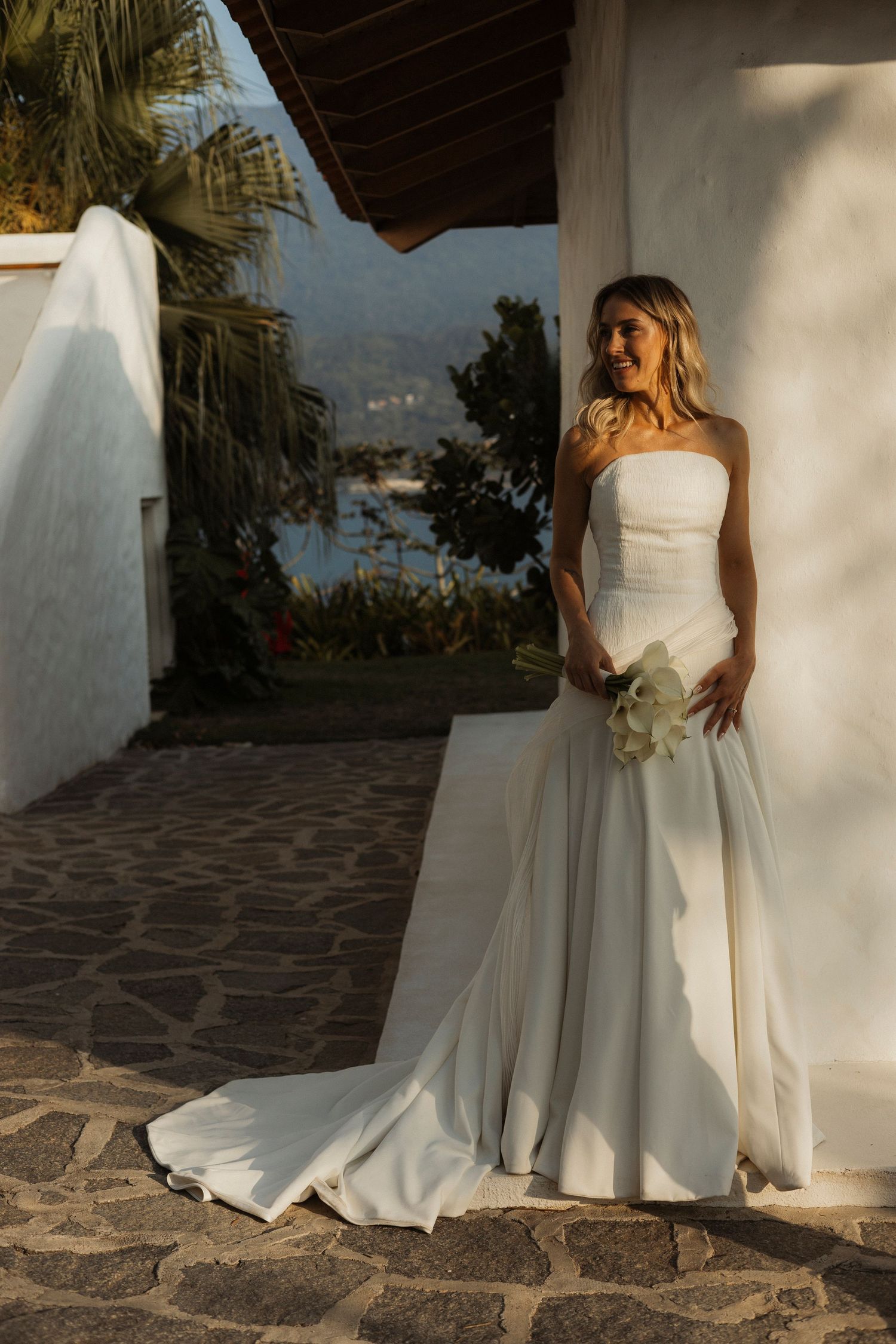 A bride in a flowing white gown poses along a stone pathway with mountain views.
