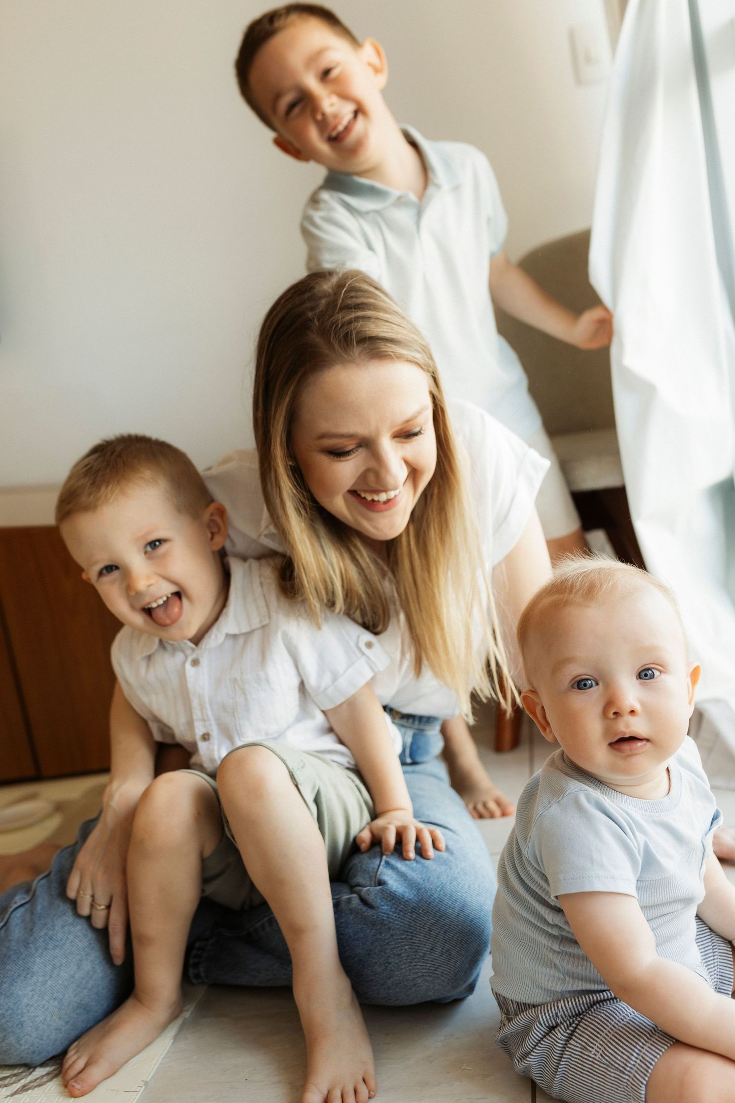 Happy young mother sitting on floor with three sons, smiling together in a bright, cozy room.