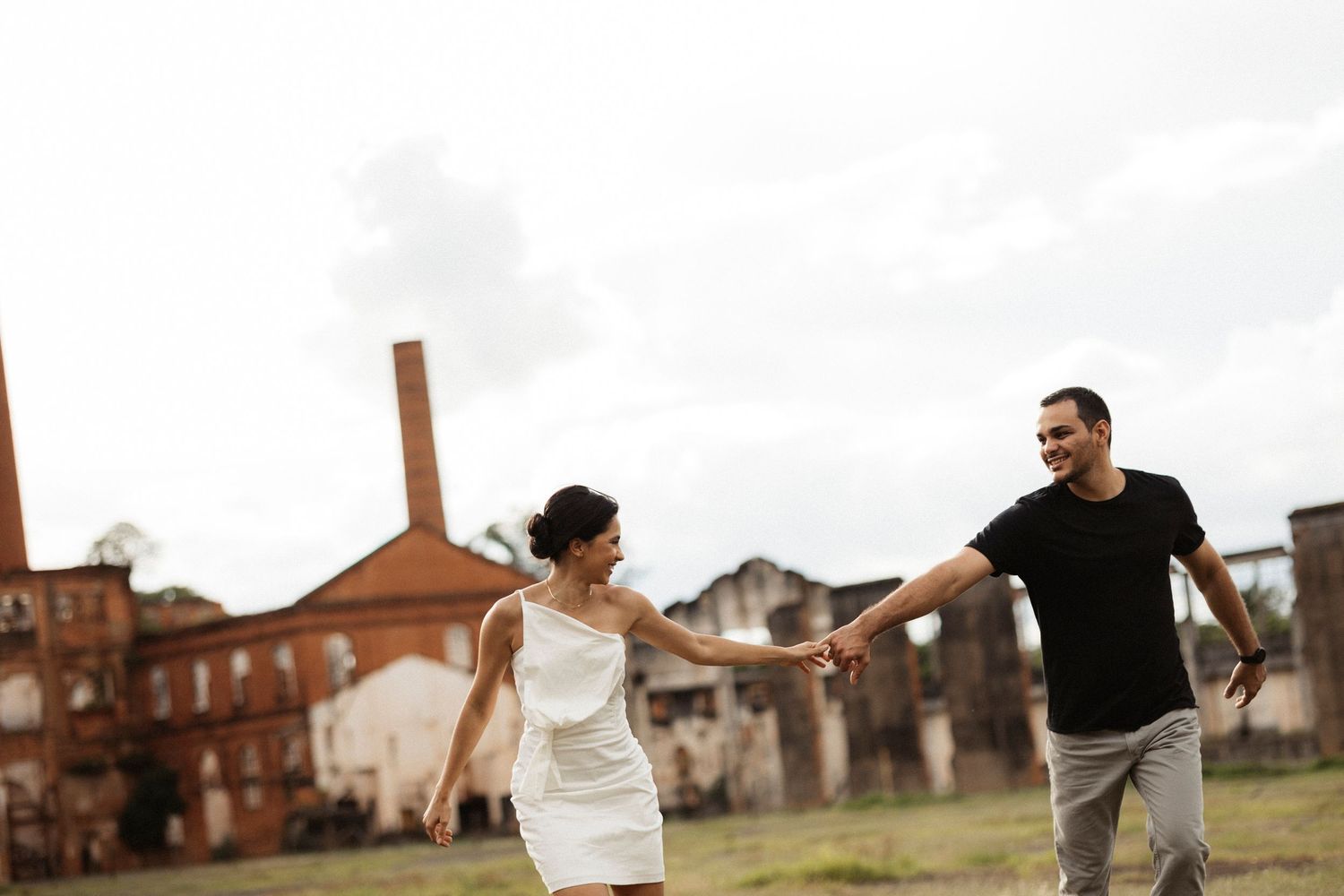 A couple in black and white attire dance and play in front of an industrial backdrop.