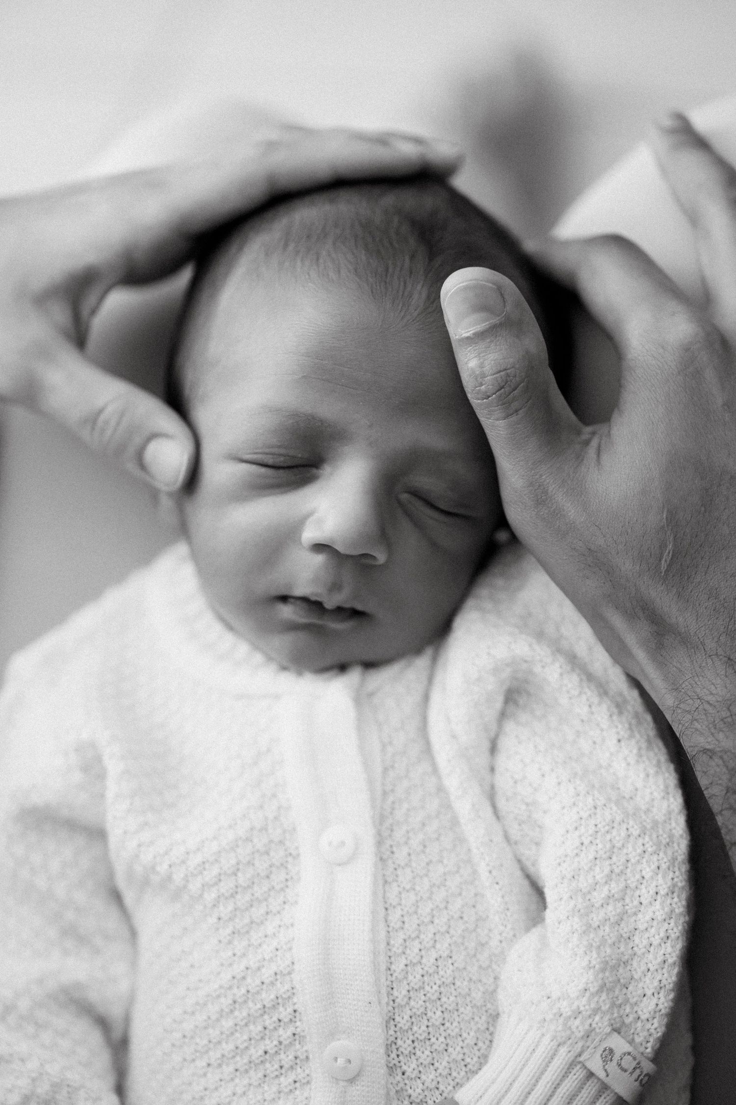 A peaceful sleeping newborn baby swaddled in white textured fabric in a black and white photograph.