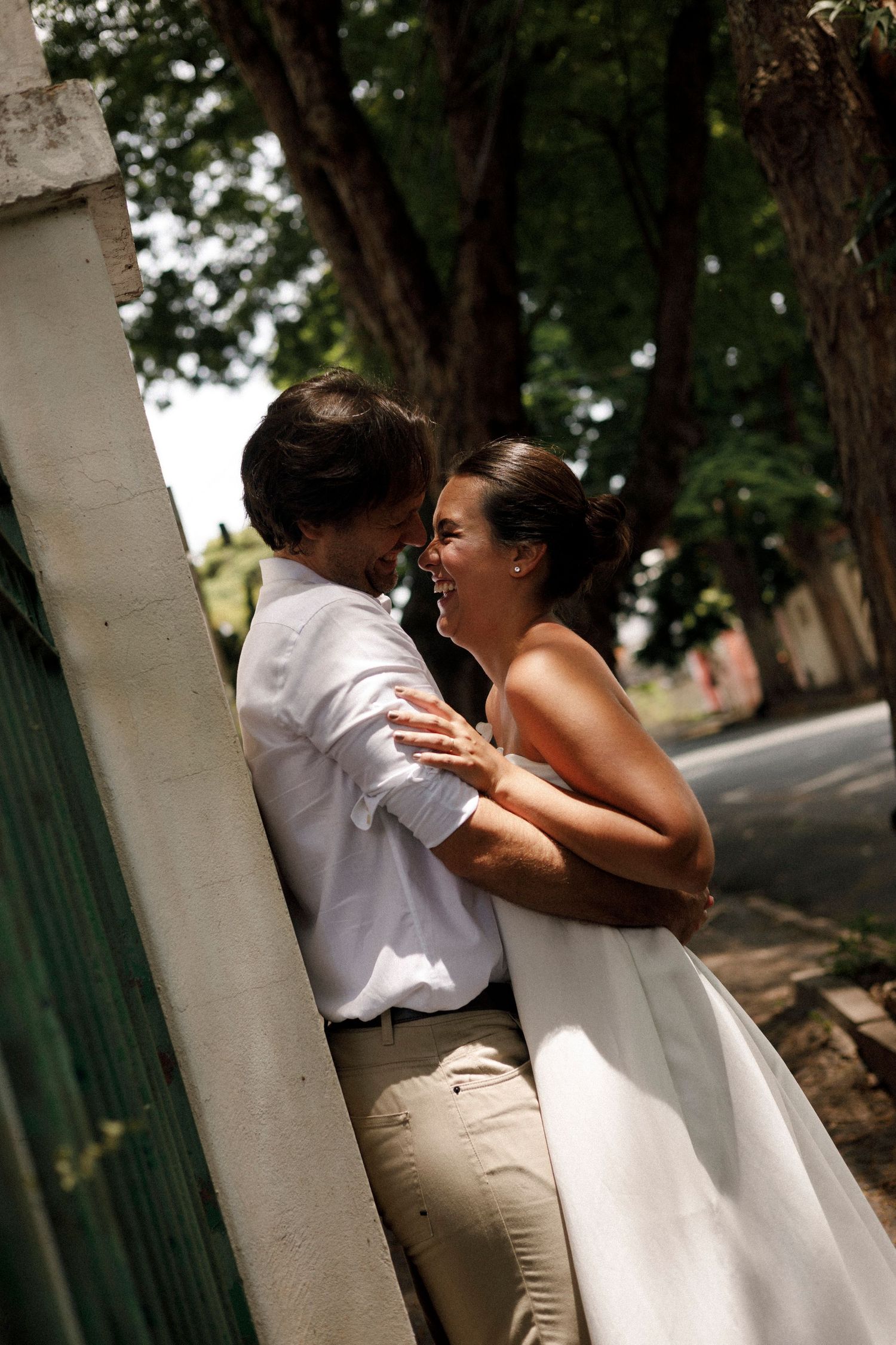 A romantic moment between newlyweds against a white pillar outdoors.