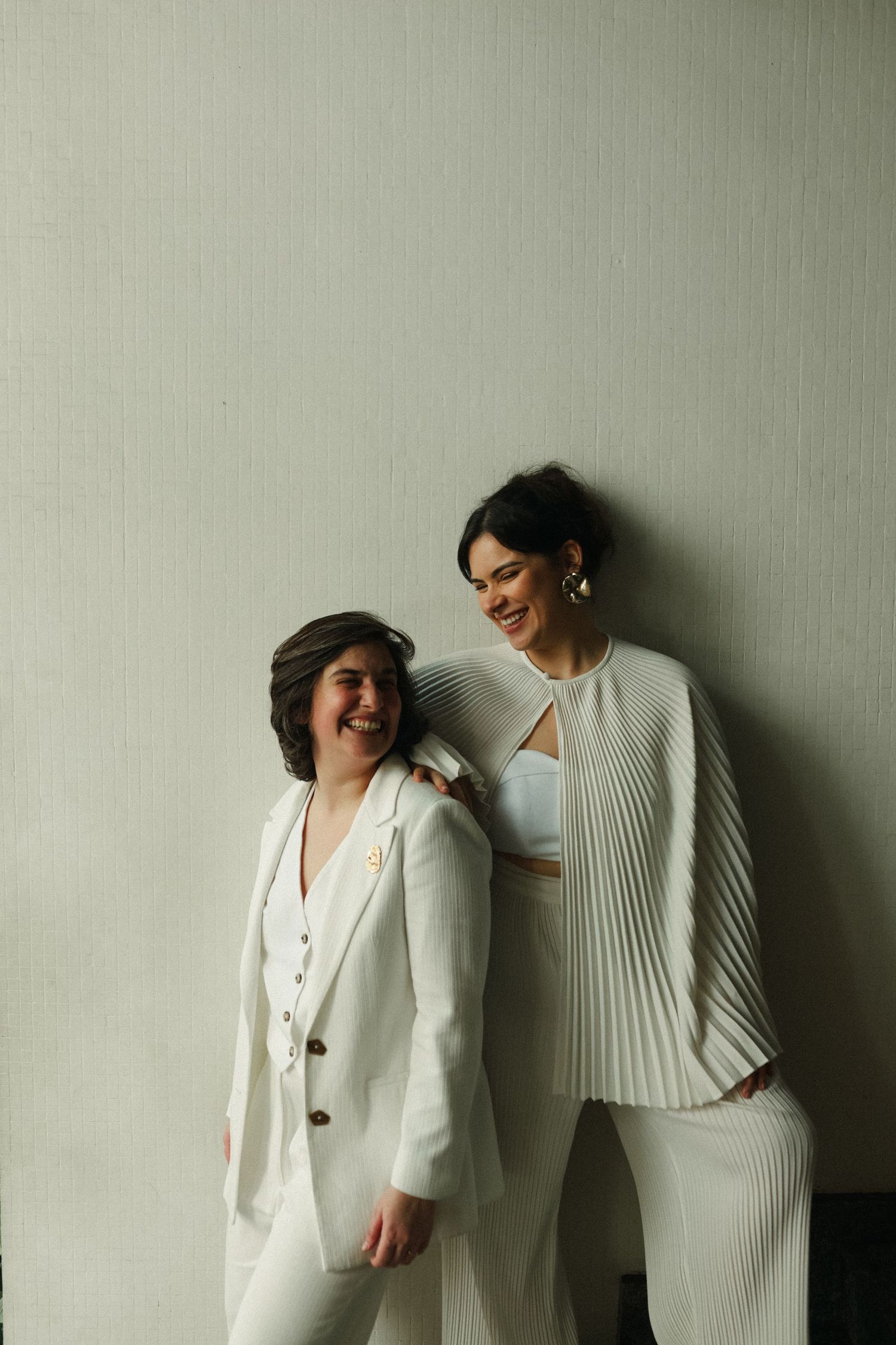 Black and white portraits against wall showing two people in white outfits sharing joyful moments.