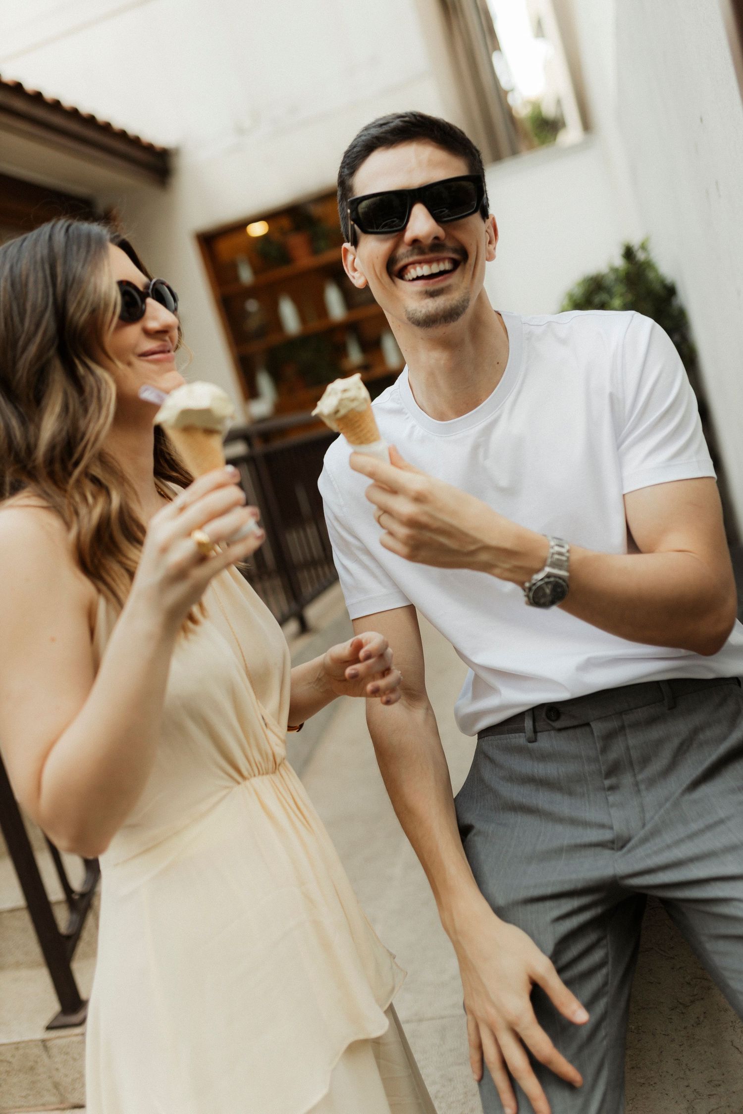 Couple enjoying ice cream cones together while wearing sunglasses on a sunny day.