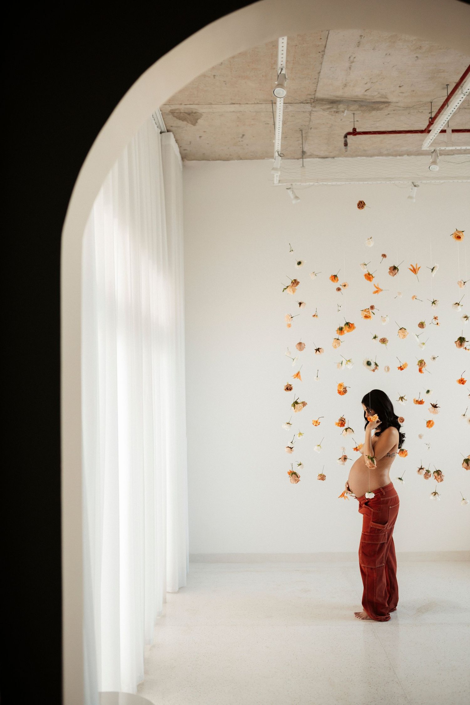 Figure in red dress interacts with hanging orange flower petals in white minimalist space.