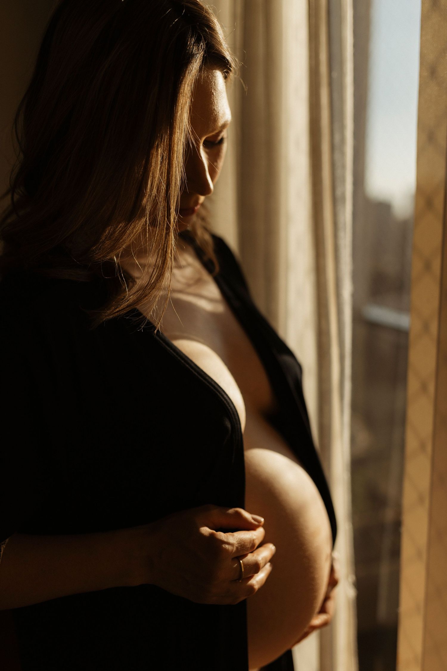Intimate boudoir photography with dramatic window lighting and shadows.