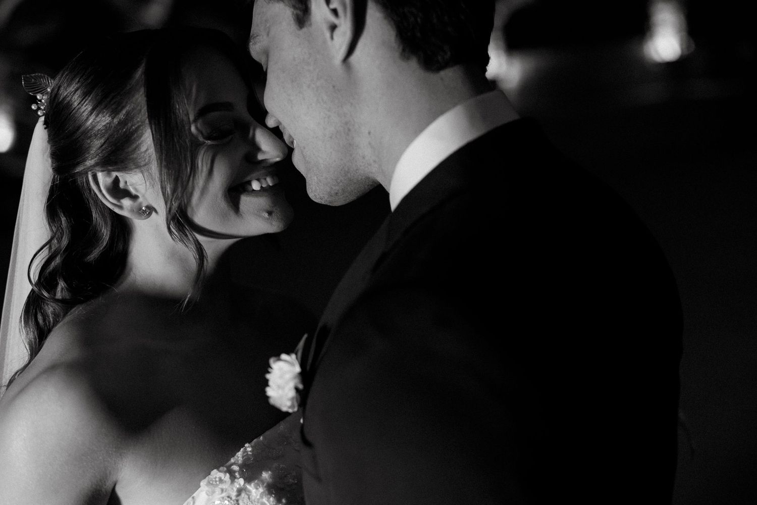 Black and white wedding photo of smiling bride and groom sharing an intimate moment, nearly kissing.