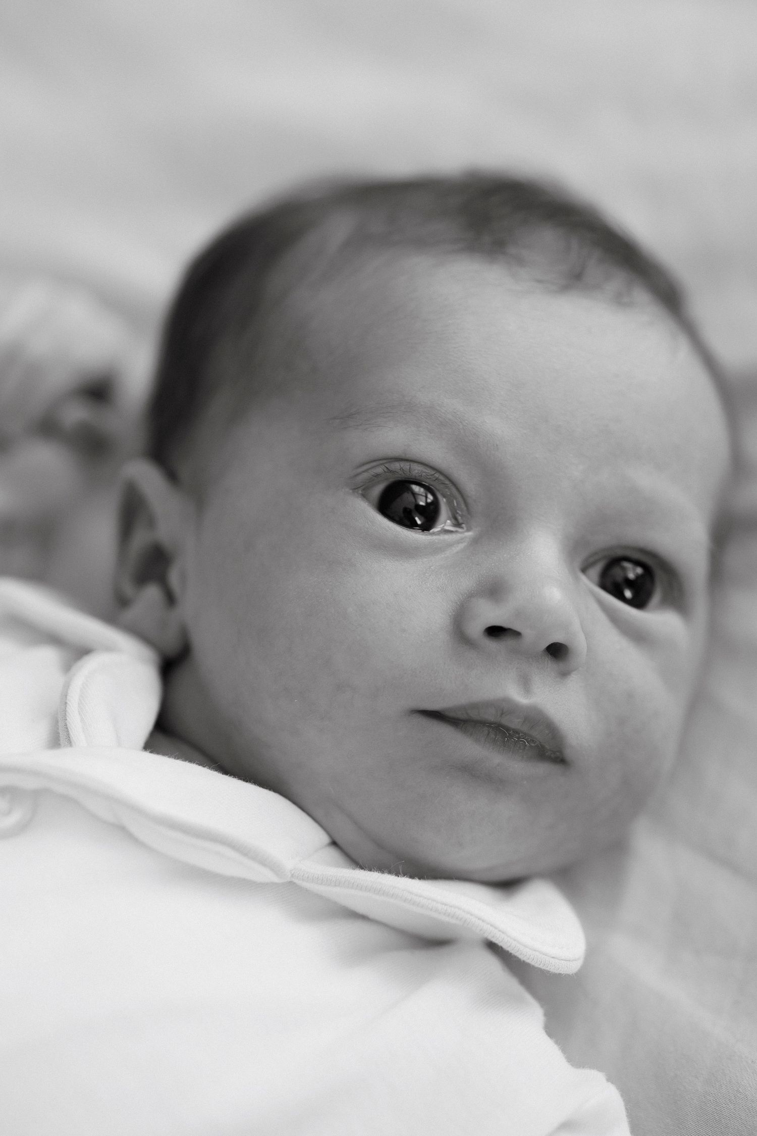 Black and white close-up portrait of a newborn baby with wide eyes, wrapped in a white blanket.