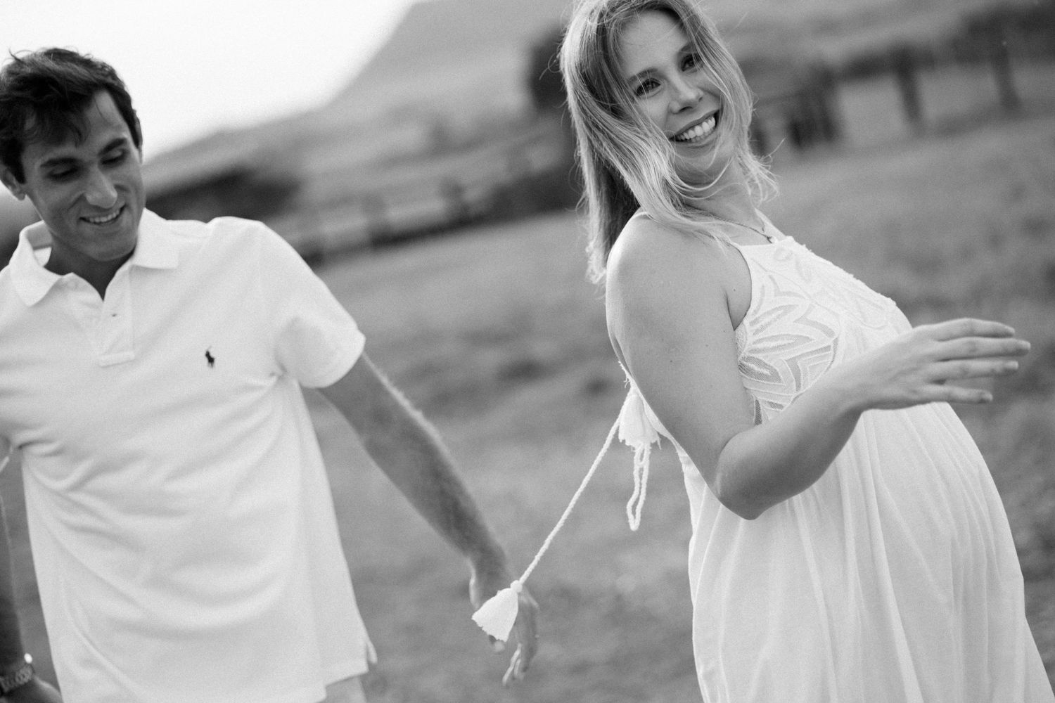 Outdoor maternity photoshoot with people wearing white clothing in natural light.