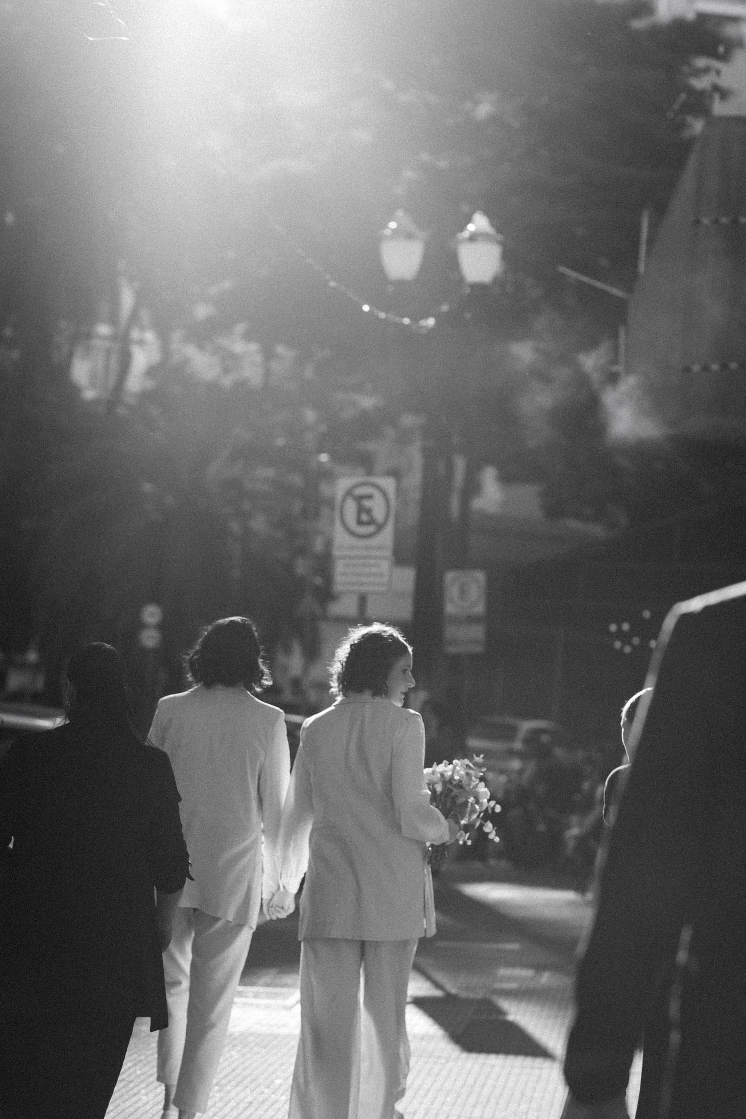 A black and white photo of two people walking together on a sunlit street.