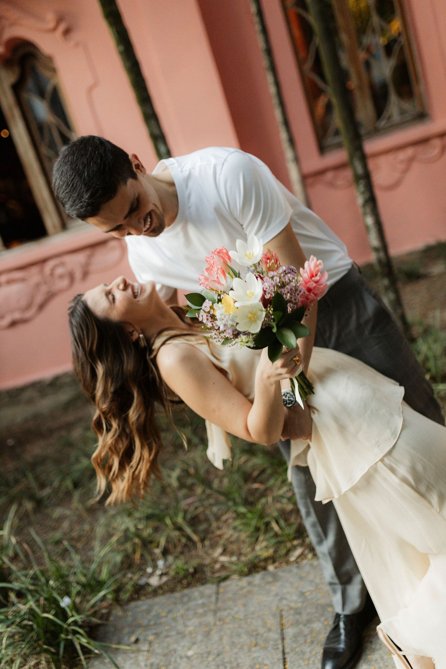 Romantic dip pose with flowers against pink wall outdoors.