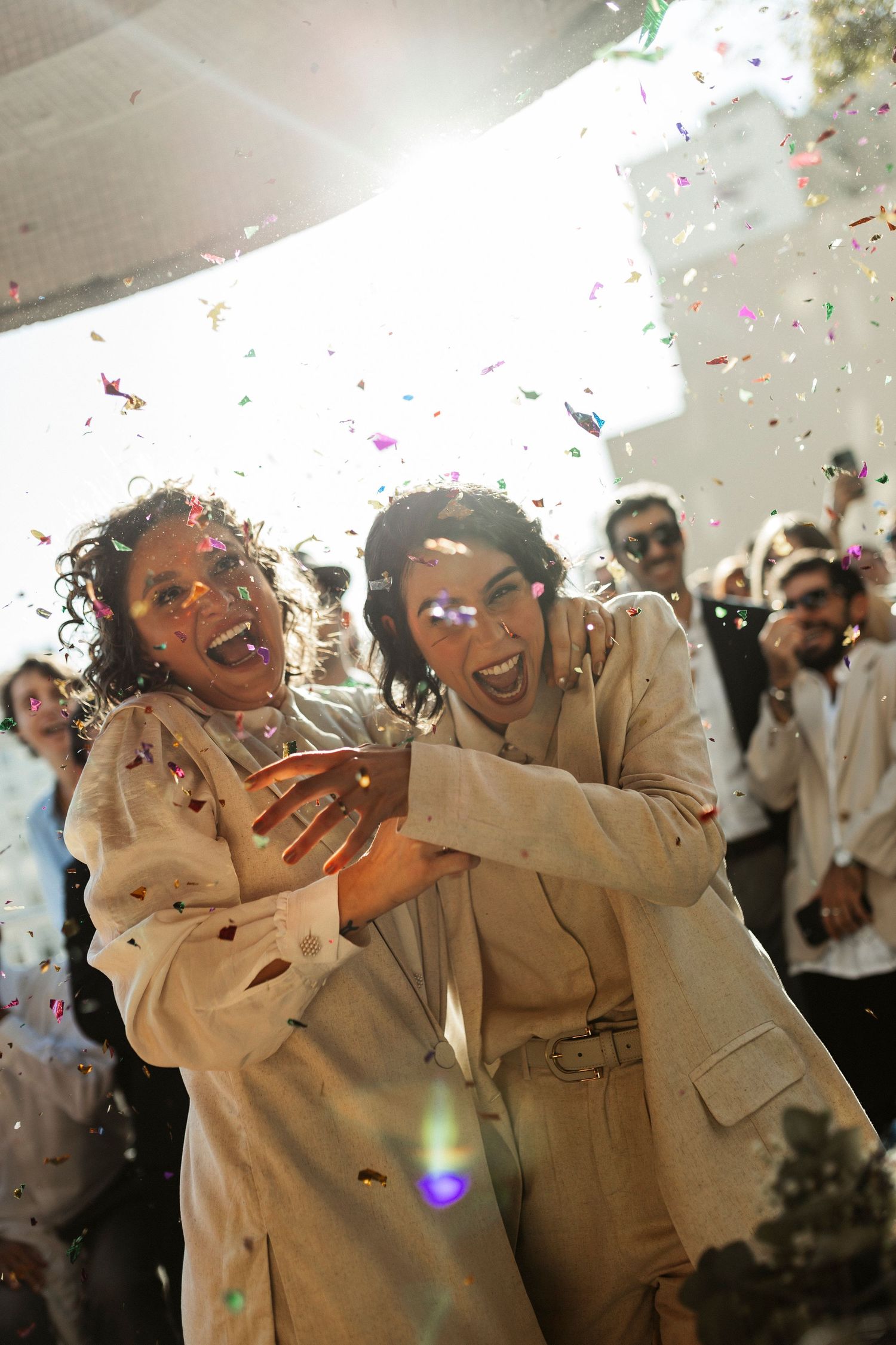 Joyful celebration with confetti falling as people in white outfits embrace and laugh.