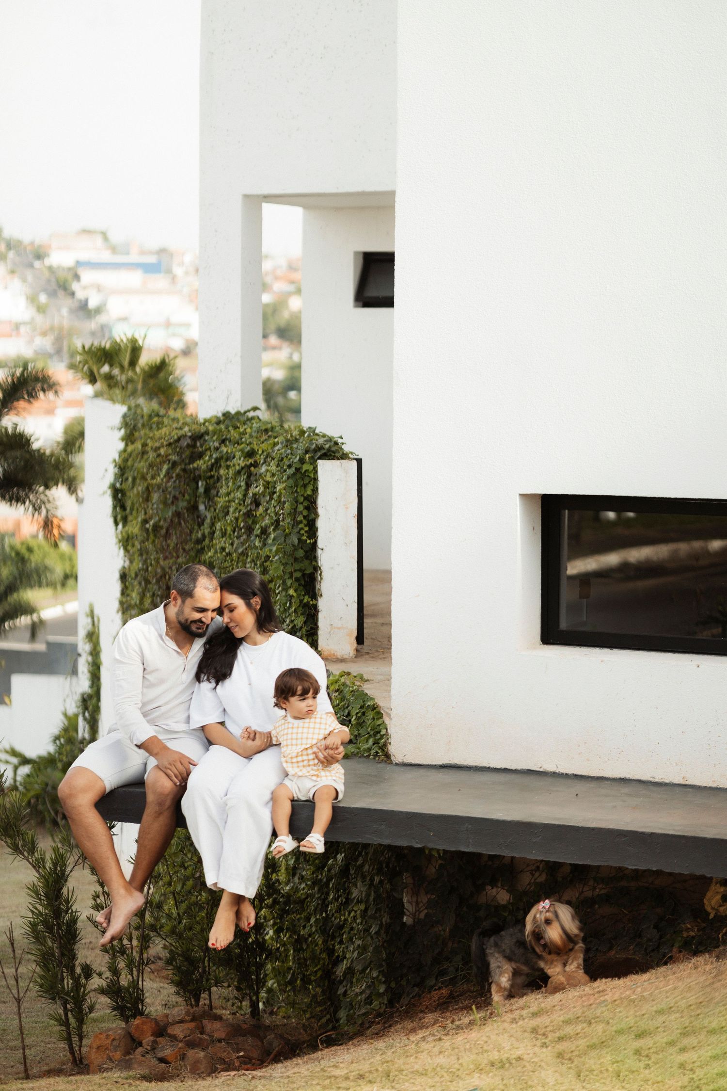 Family sitting together outdoors on modern white architecture surrounded by greenery.