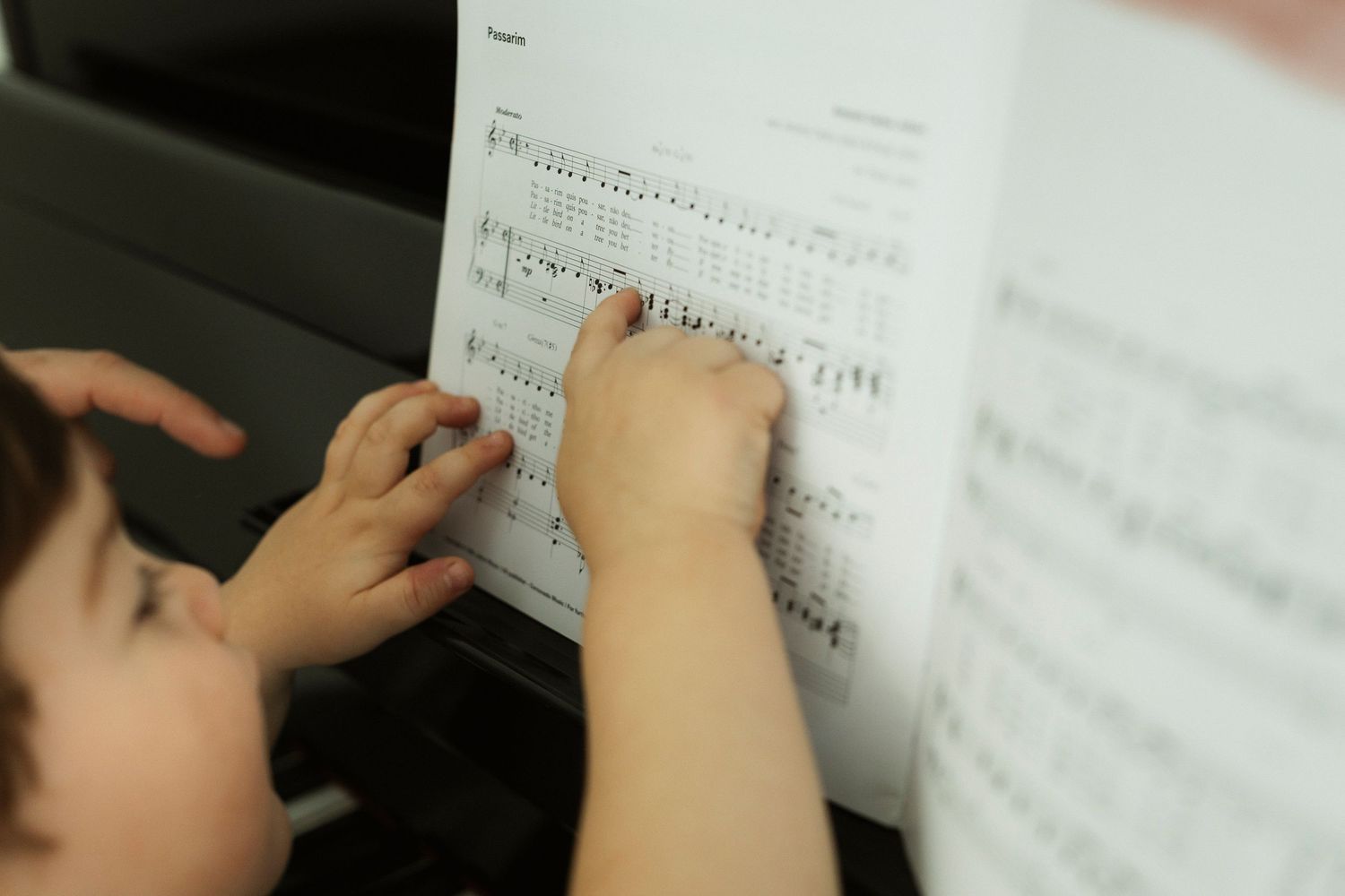 Child and adult hands pointing at sheet music on a piano, learning to read musical notes together.
