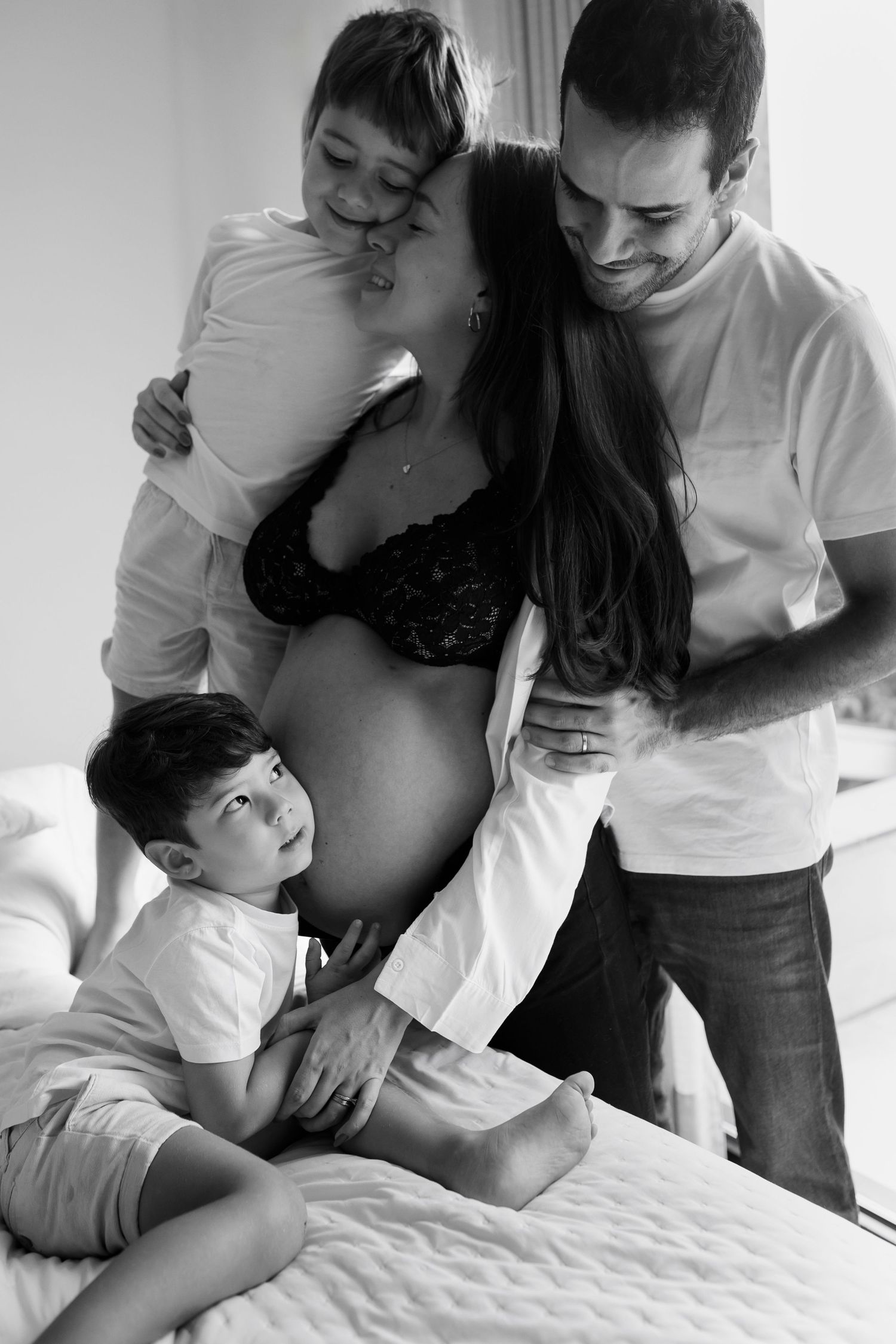 Black and white family maternity session showing tender moments on bed.