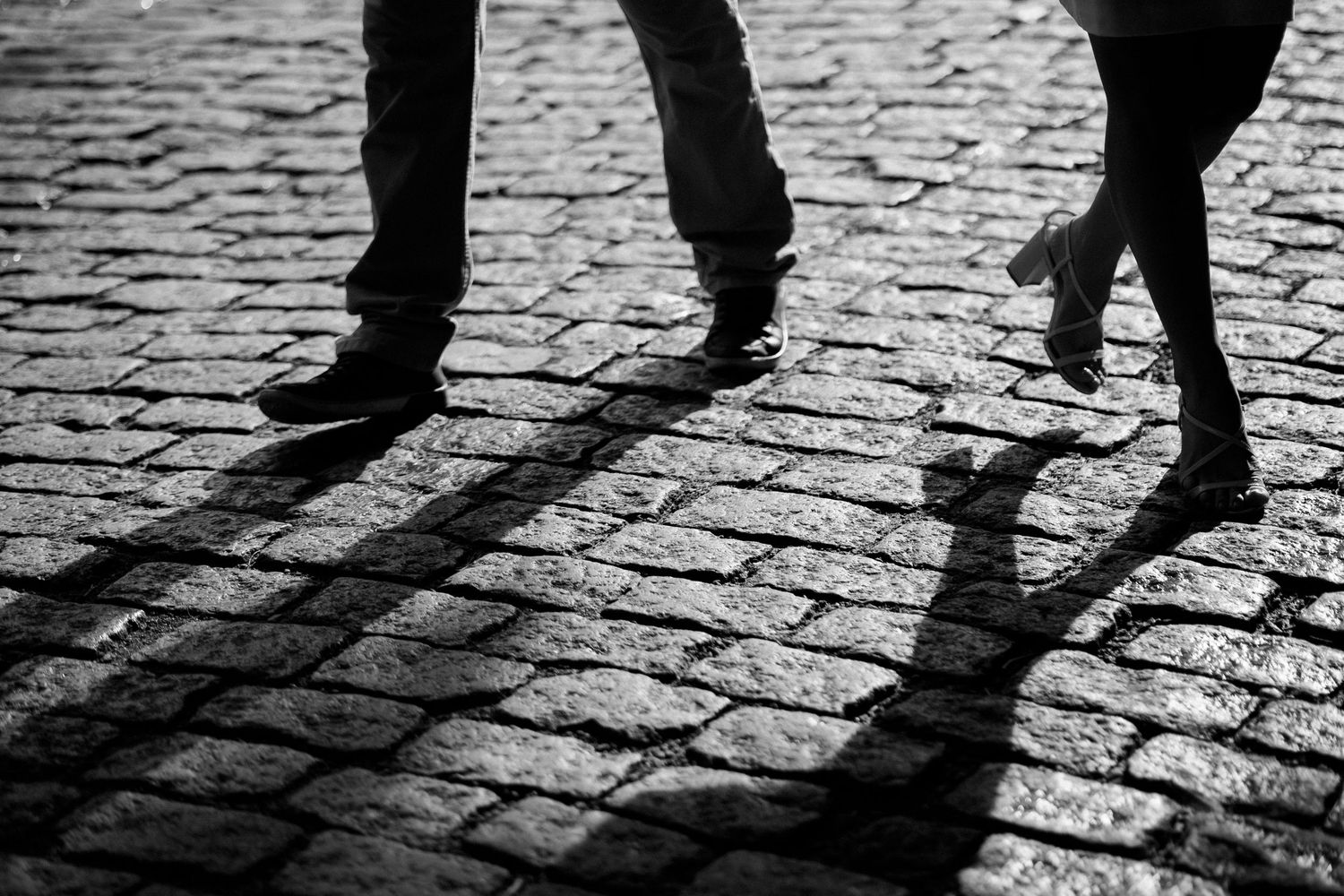 Shadow patterns of feet on cobblestone pavement during a romantic photoshoot.