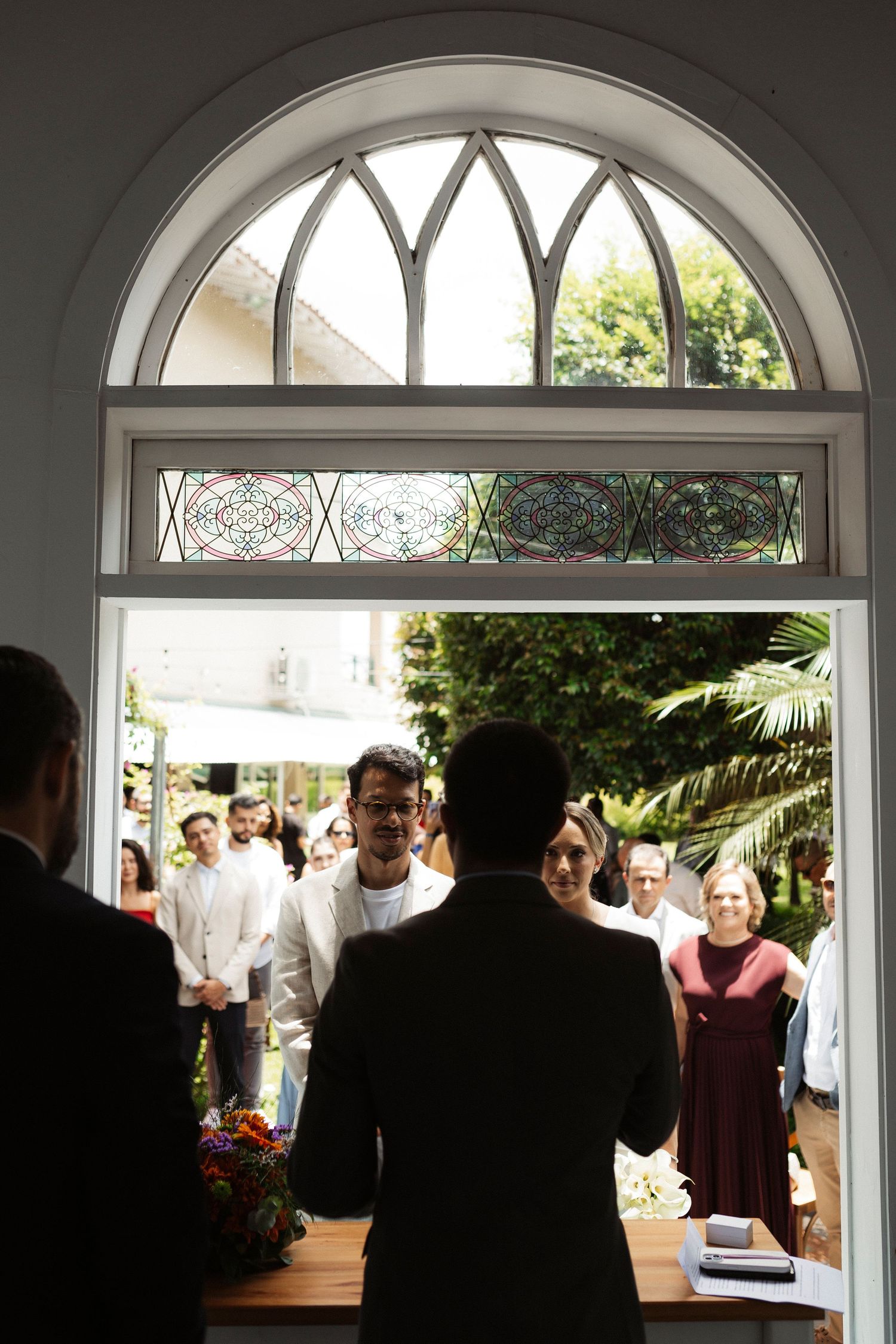 Wedding ceremony guests gather under arched doorway with stained glass details.