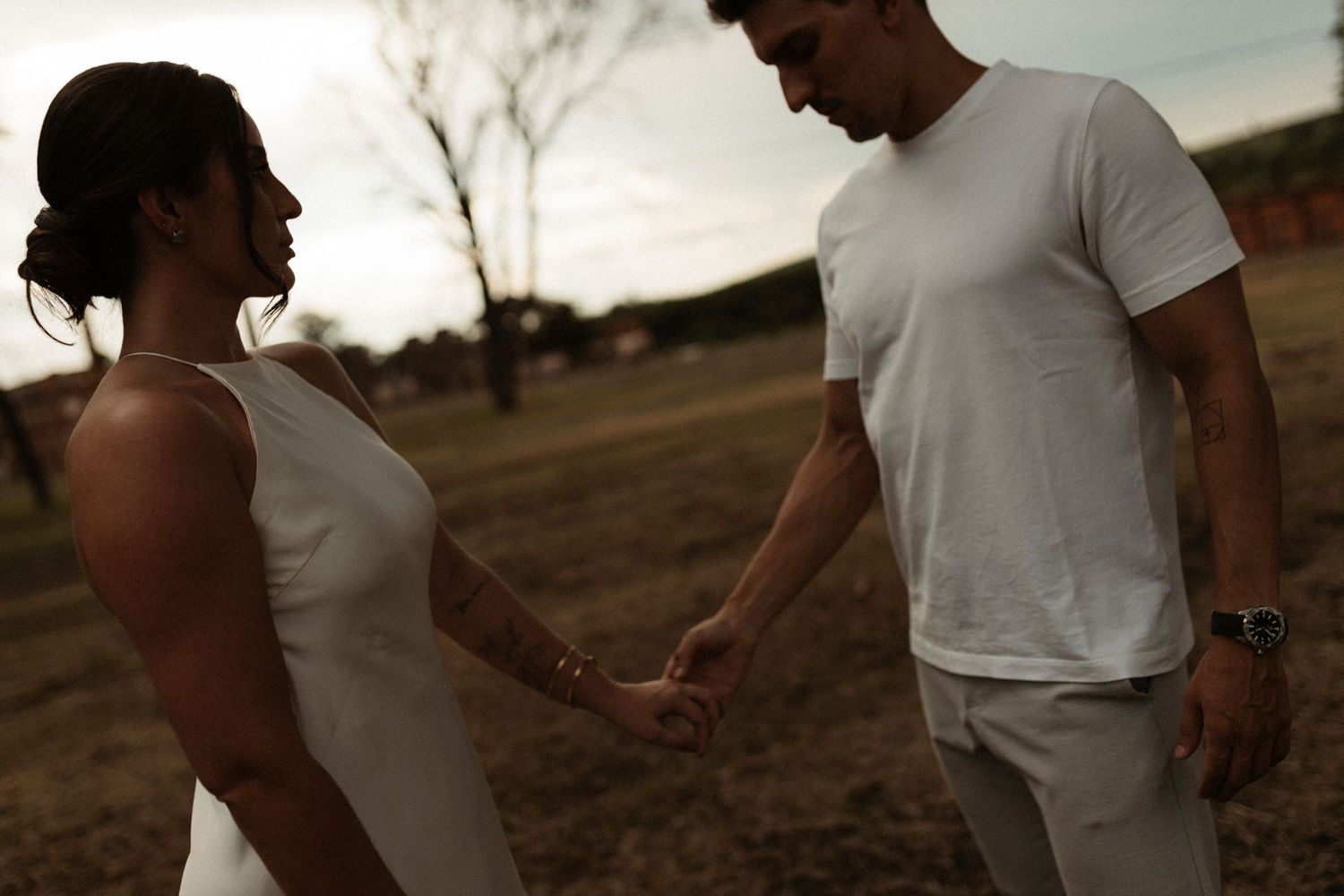 Couple in white clothing sharing tender moments at sunset in a natural setting.